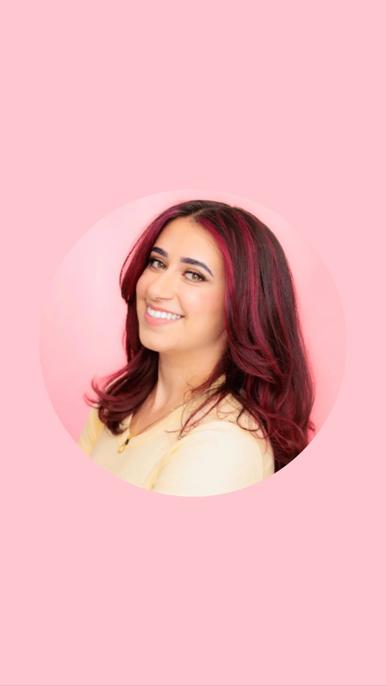 A woman smiling and sitting on the ground, wearing a black hat, a black lace dress, and colorful wristbands, surrounded by people at a crowded event.