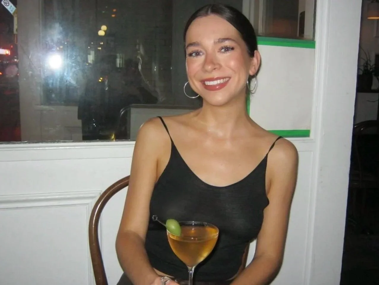 Young woman in a red dress holding spiral notebooks, standing against a white brick wall.