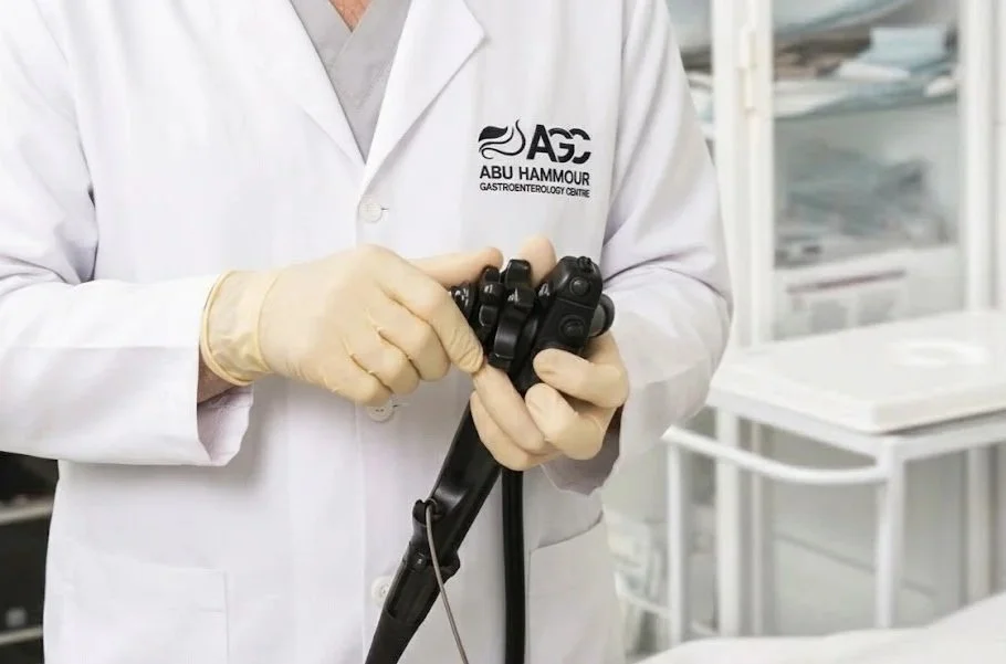 Close-up of a medical professional holding an endoscope in a clinical setting, wearing gloves and a white coat with a logo for Abu Hammour Gastroenterology Center.