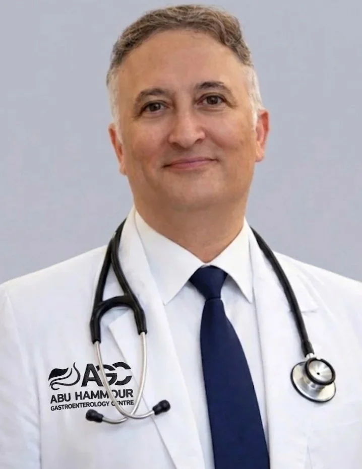 A middle-aged male doctor with gray hair, wearing a white lab coat with a logo that reads 'ABU HAMMOUR GASTROENTEROLOGY CENTRE', a navy blue tie, and a stethoscope around his neck, smiling and looking at the camera.