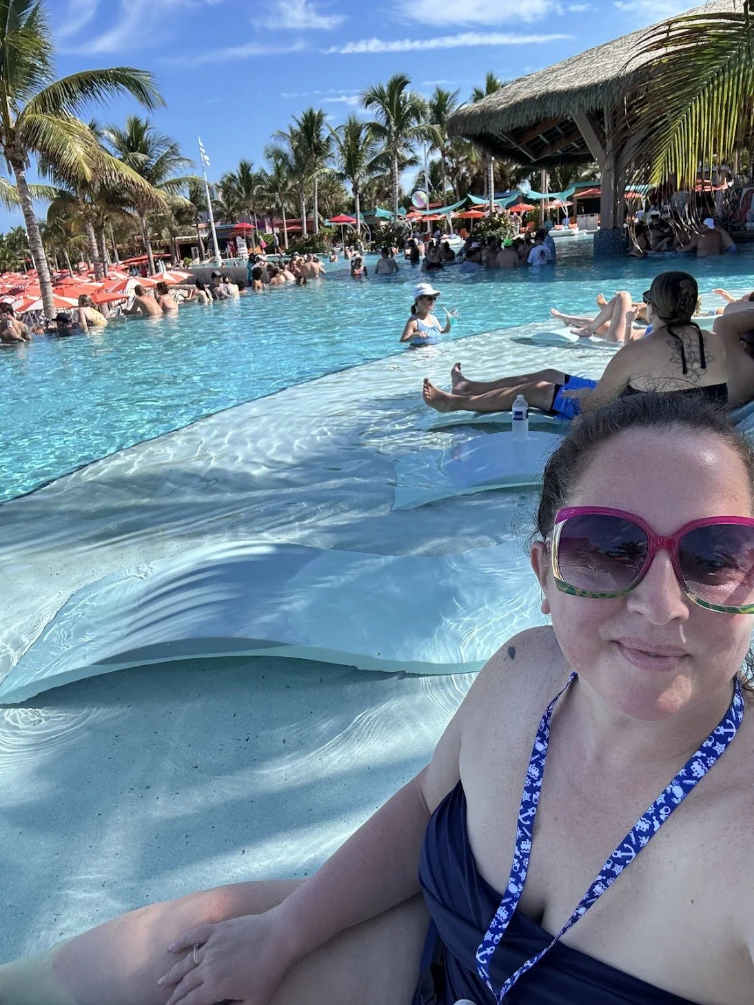 Celeste Woodside, cruise travel advisor, relaxing in the pool at Hideaway Beach on Perfect Day at CocoCay, surrounded by palm trees, turquoise water, and the lively adults-only beach club atmosphere in the Bahamas.