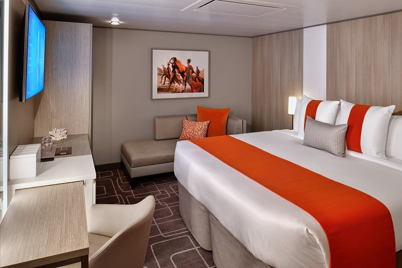 Contemporary interior stateroom on the Celebrity Beyond with a king bed, sofa, desk, and modern furnishings aboard a cruise ship.