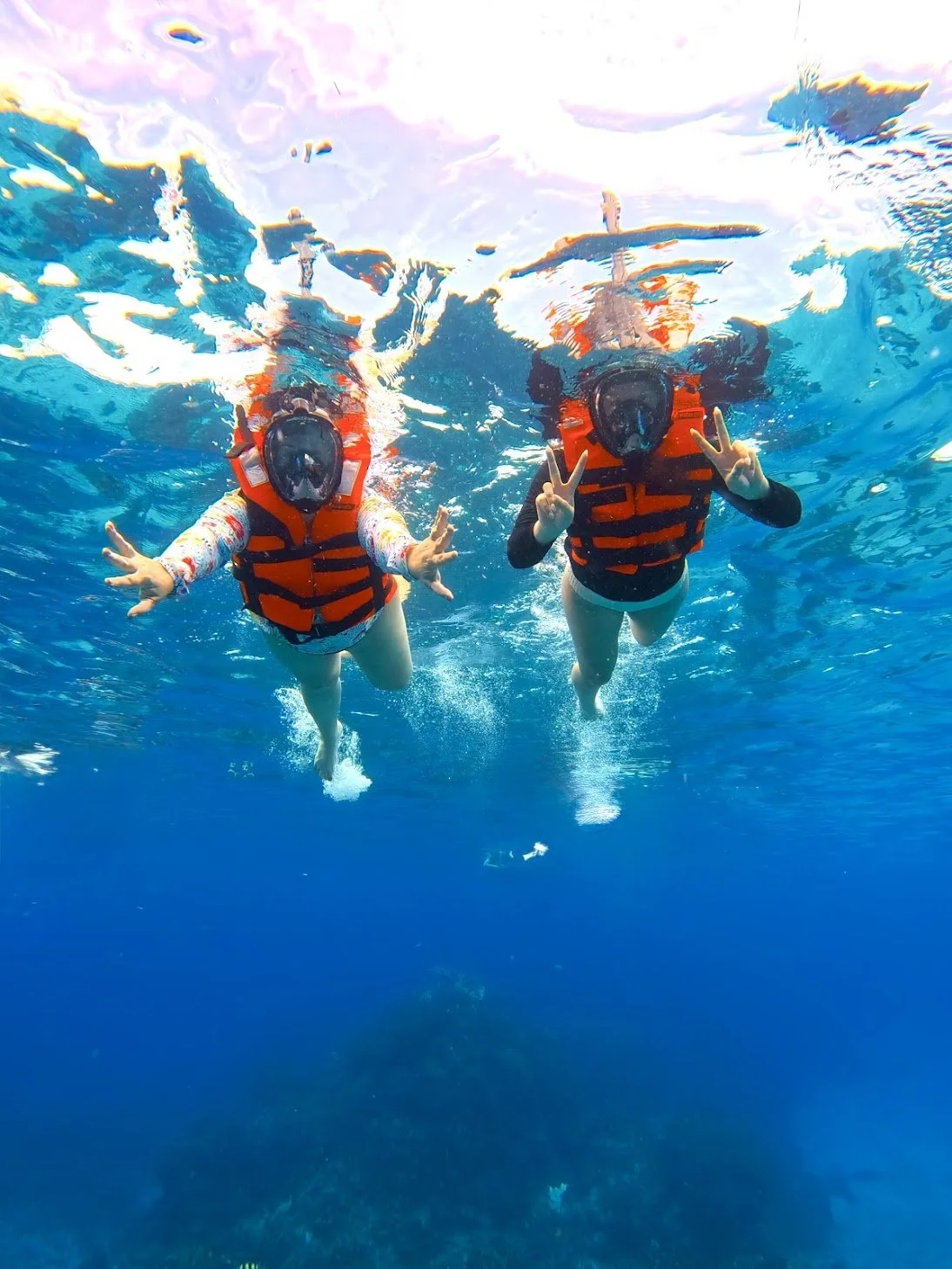 Two travelers snorkeling underwater in the Caribbean Sea wearing orange life jackets and full-face snorkel masks during a Cozumel excursion.