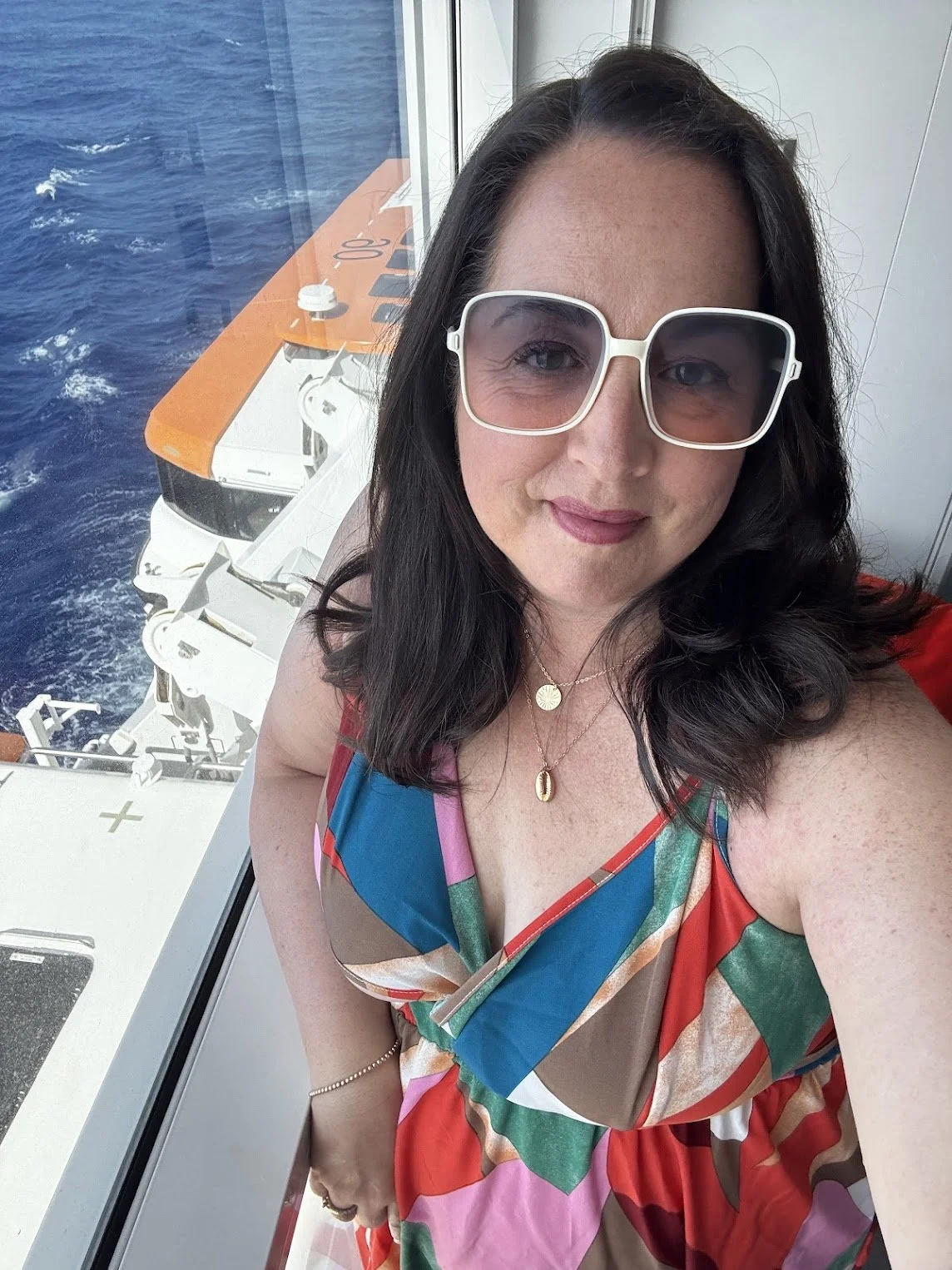 Celeste Woodside, travel advisor on a cruise ship balcony wearing white sunglasses and a multi-colored dress.