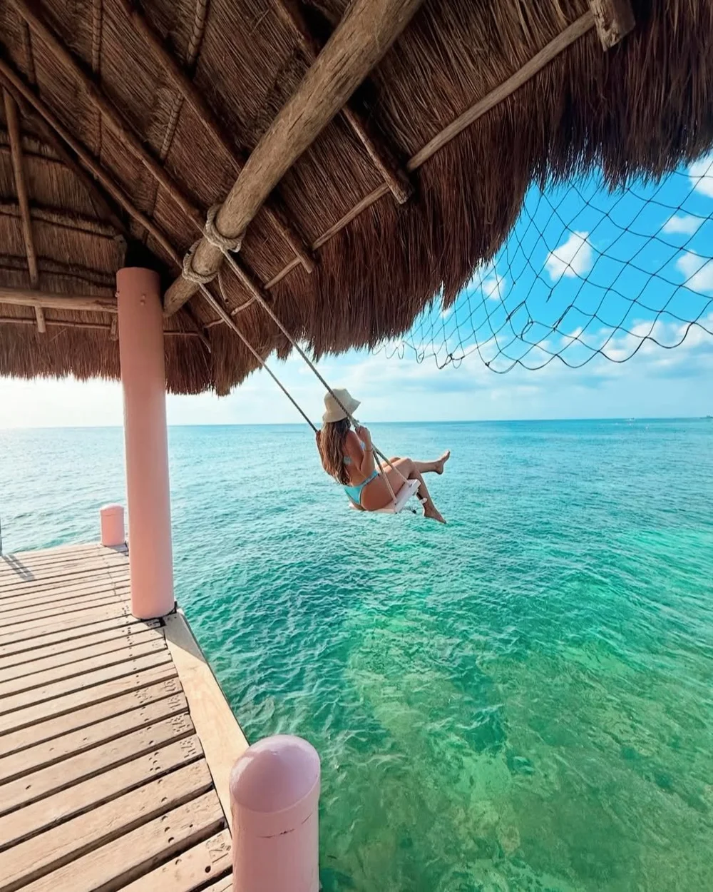 Woman on a swing over the clear water at a Cozumel beach club