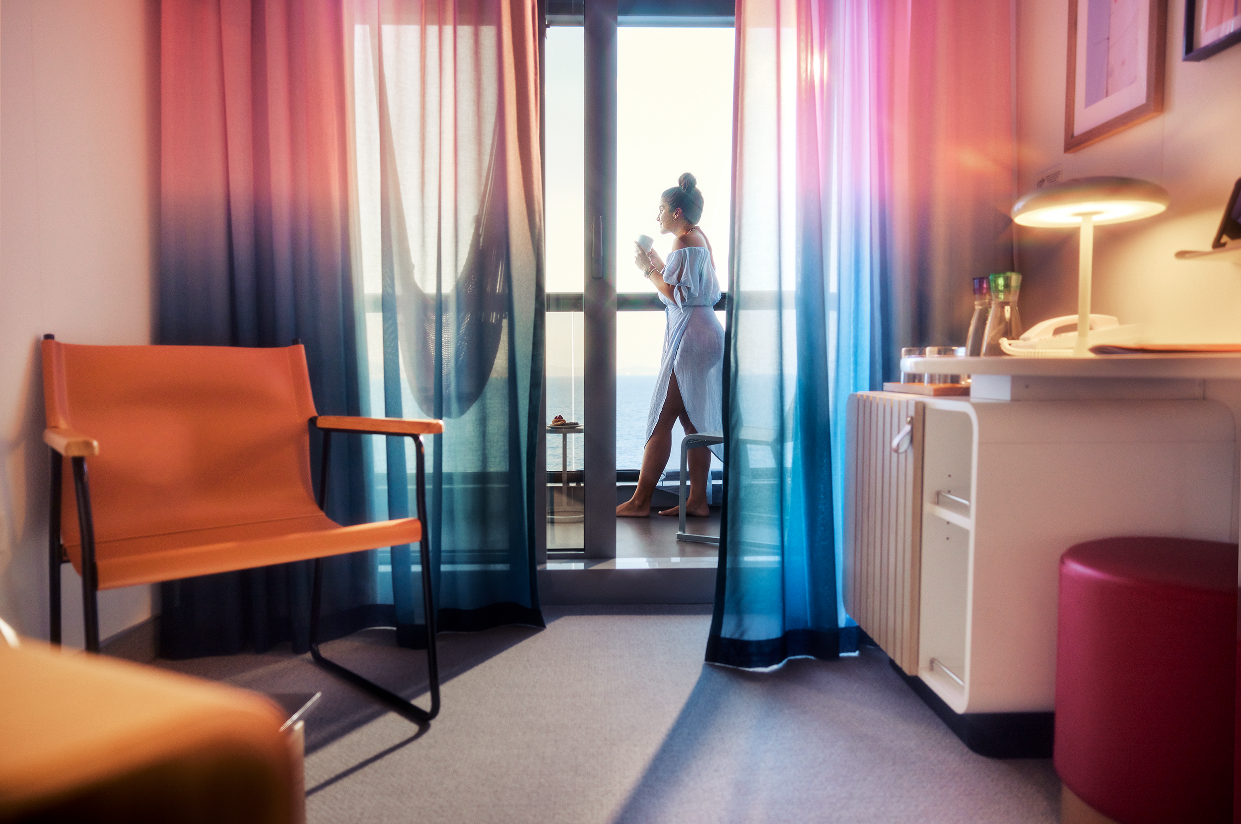 Woman with morning coffee looking out at the ocean from a Virgin Voyages cabin balcony — stylish staterooms designed for adults on a Virgin Voyages cruise