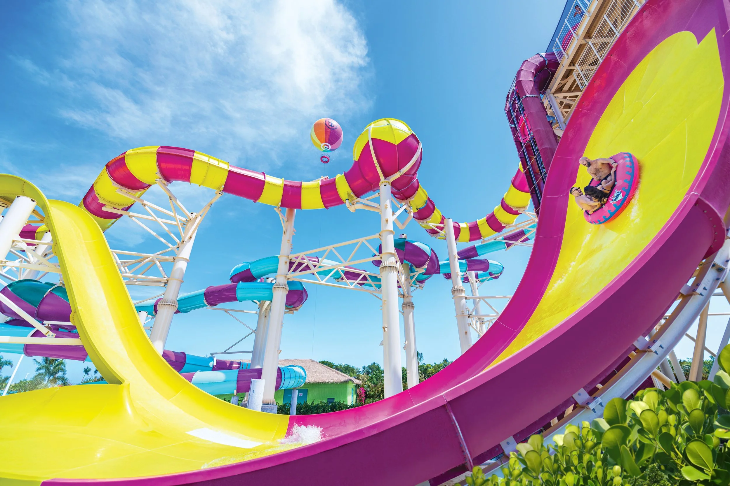 Bright yellow and pink waterslides at Thrill Waterpark on Perfect Day at CocoCay in the Bahamas, with riders splashing through a large curved slide under a blue sky on Royal Caribbean’s private island.