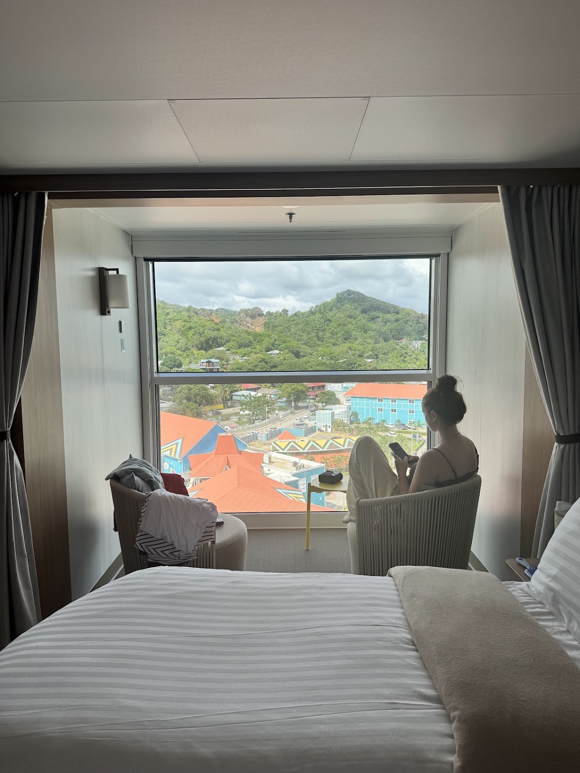 Infinite veranda cruise cabin on Star of the Seas with a large picture window, comfortable seating, and panoramic views of a Caribbean port.