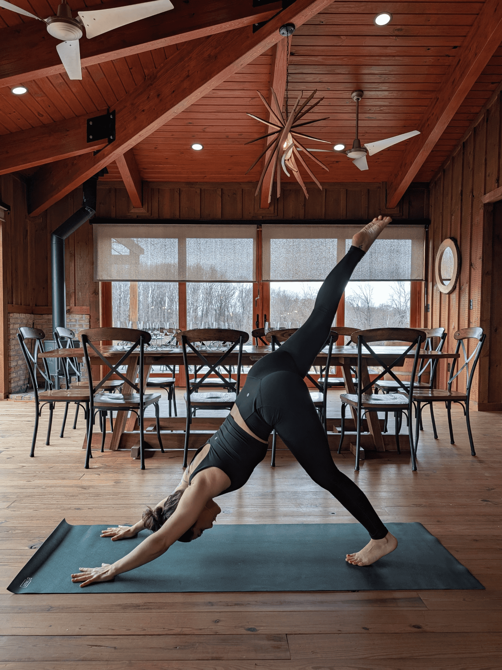 Group of people practicing yoga outdoors on a sunny day, performing a side stretch pose on yoga mats on grass with trees and a pavilion in the background.