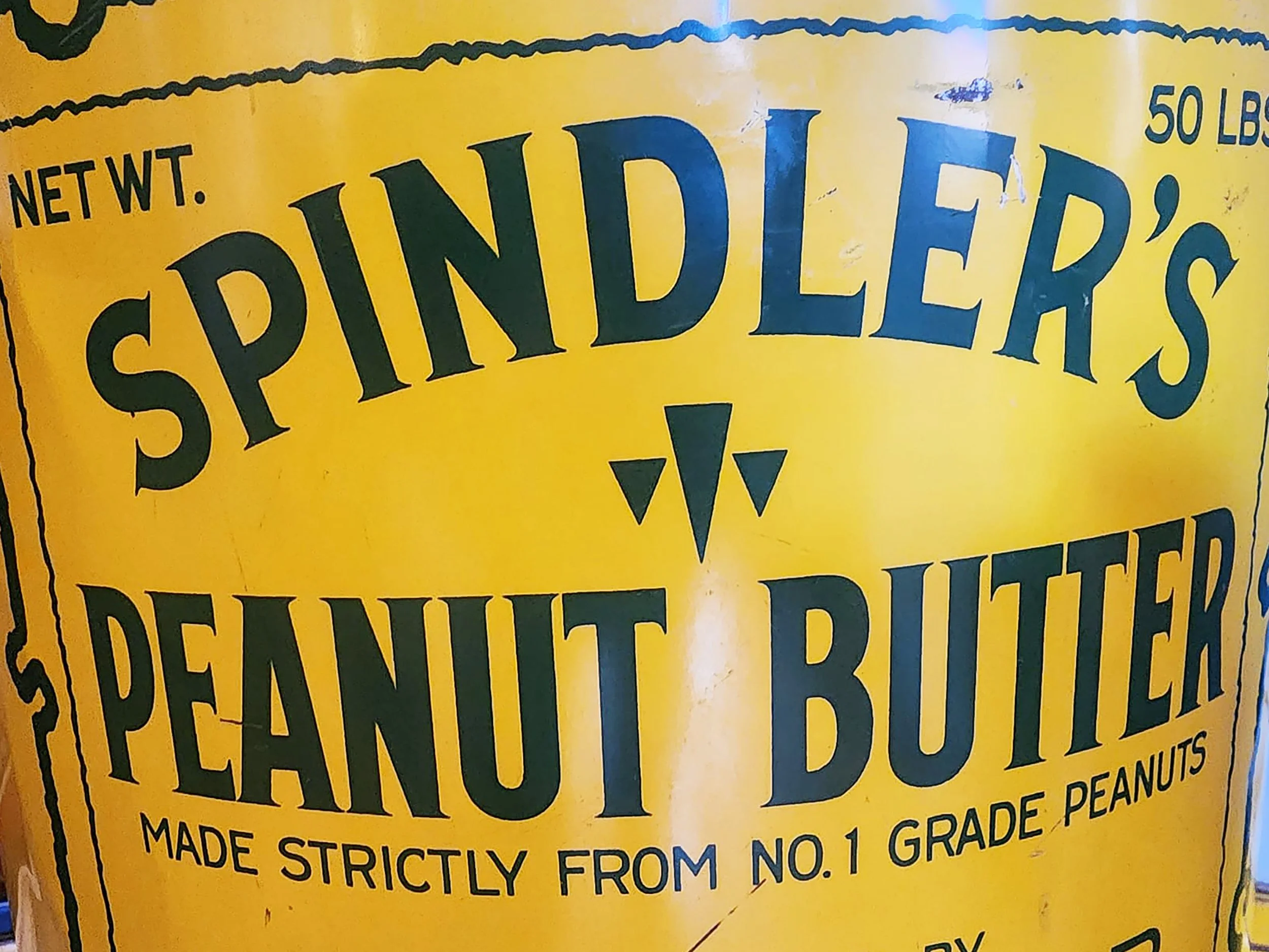 Close-up of a yellow Spindler's Peanut Butter tin, with black and blue text, showing part of the product packaging.
