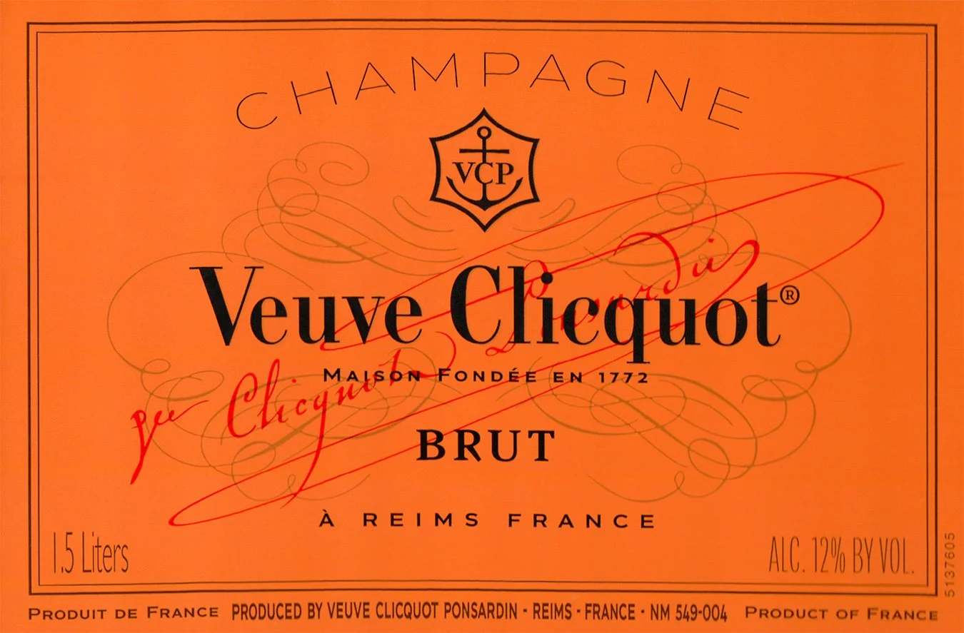 Orange champagne bottle label with black and red text, featuring the Veuve Clicquot brand, and a crest with anchor symbol, indicating 1.5 liters volume and 12% alcohol content.