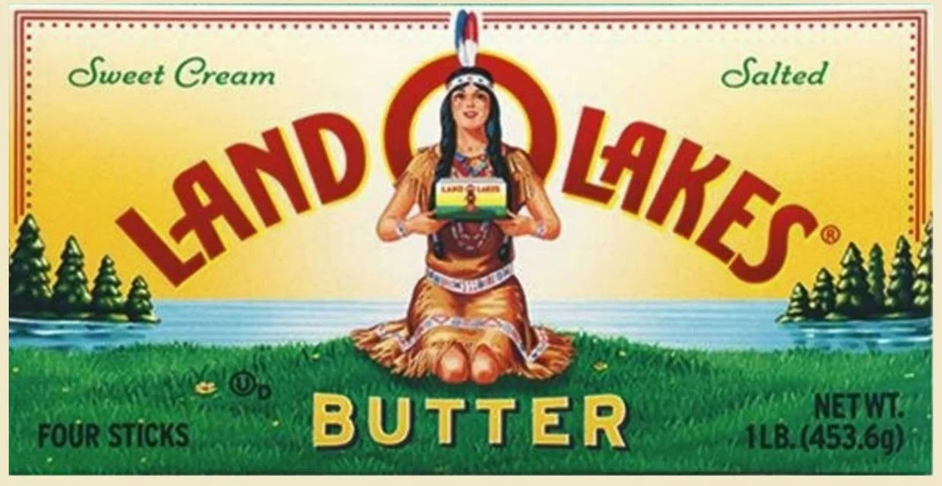 Land O'Lakes Butter package with Native American woman holding a box of butter, sitting on grass near water, with trees in the background.