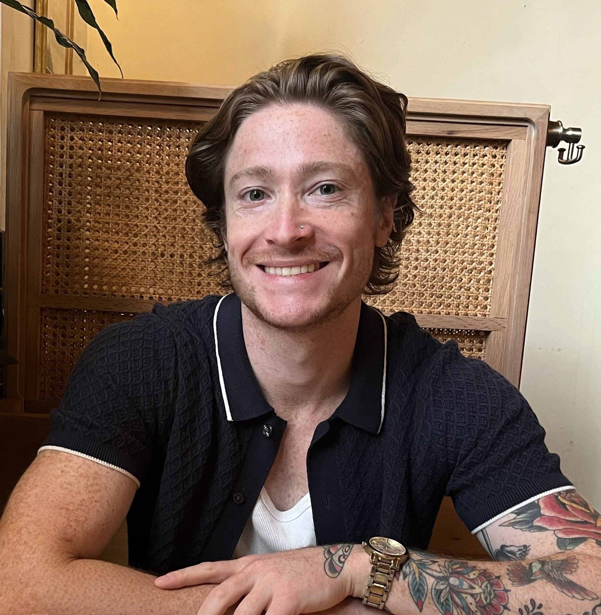 Person with glasses smiling indoors, brick wall background.