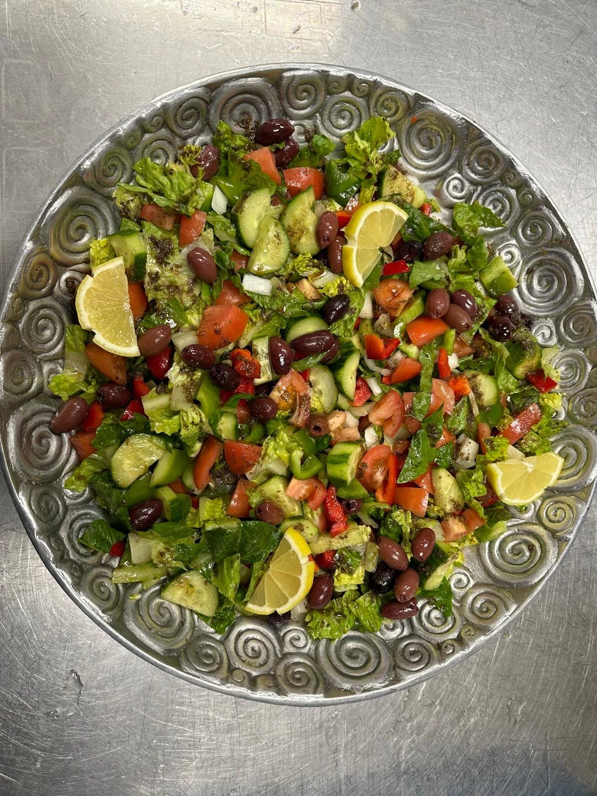 bowl of lebanese salad with cucumbers, tomatoes, onions, black olives and lemon slices