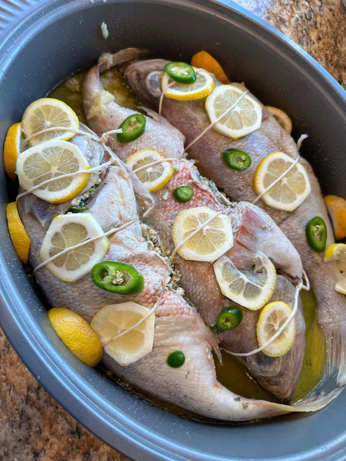 3 big fishes in a pot wrapped with herbs, lemon slices and jalapenos