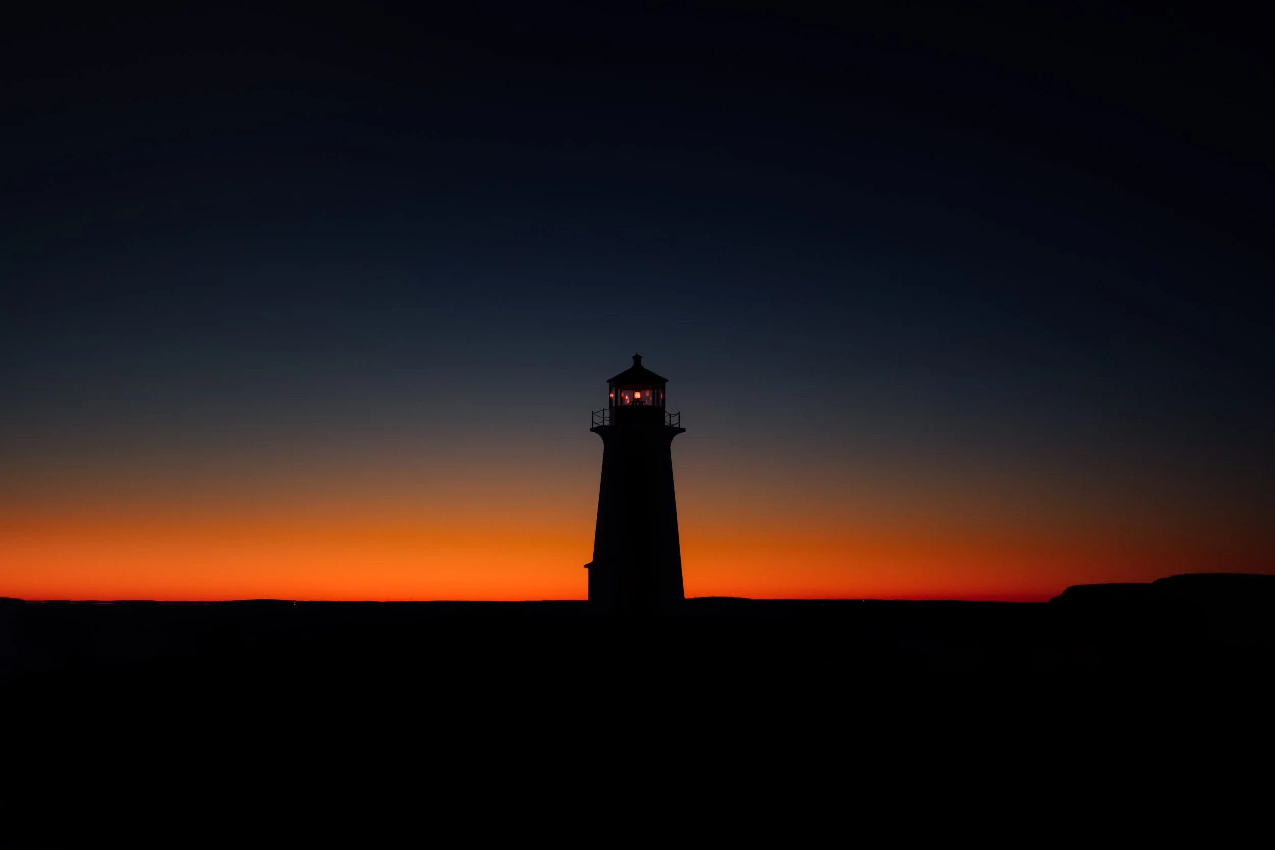 A lighthouse silhouette against a colorful sunset sky with orange, yellow, and dark blue hues.