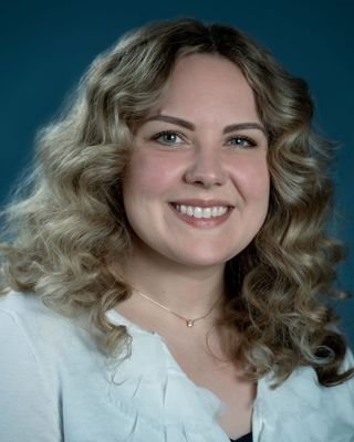 A young woman with blonde, curly hair smiling against a blue background.