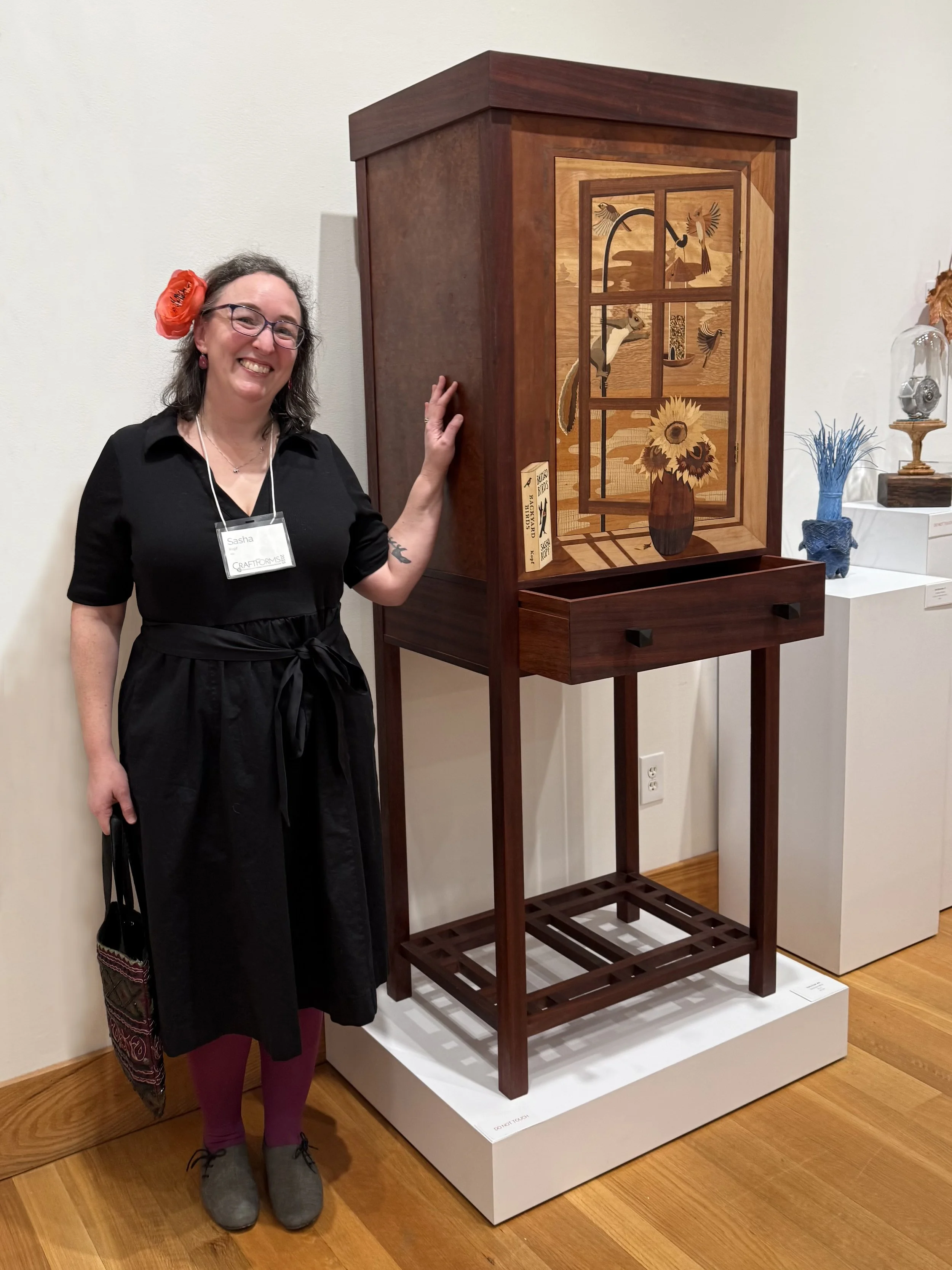 Photo of  me standing in front of my Backyard Birds cabinet at the CraftForms 2025 exhibit
