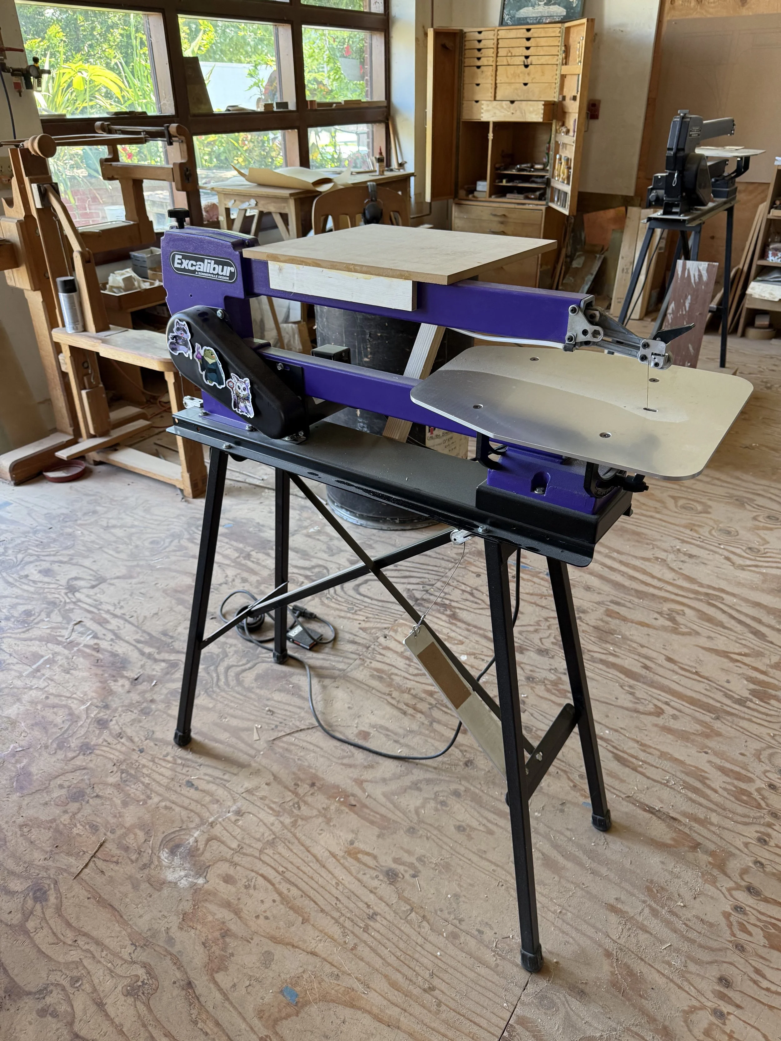 Photo of my new purple scroll saw in the woodshop with a small table clamped to it. Another older scroll saw is visible in the background.