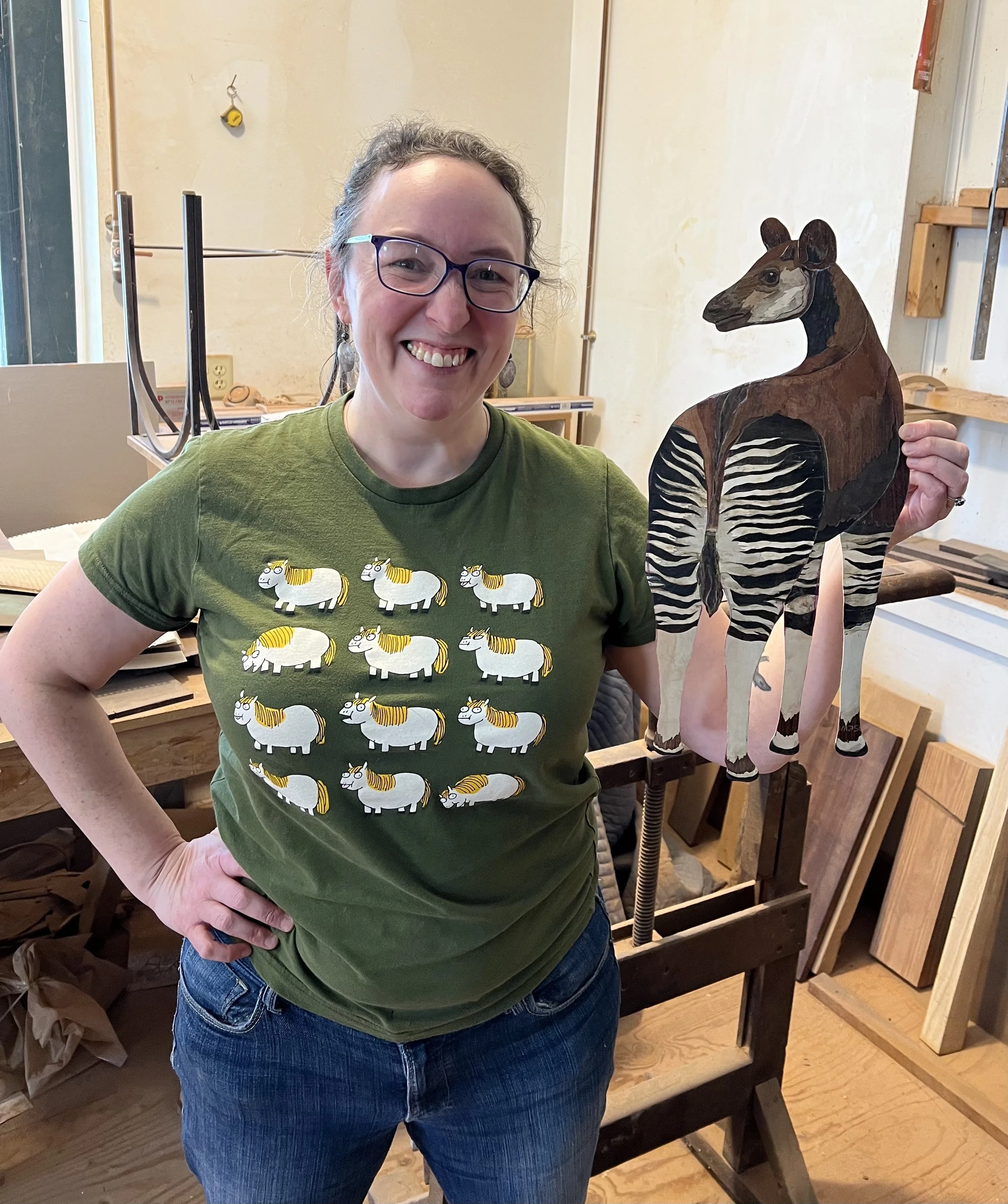 Photo of me in the woodshop, holding my marquetry okapi on the day that I cut out its shape to fit into the background