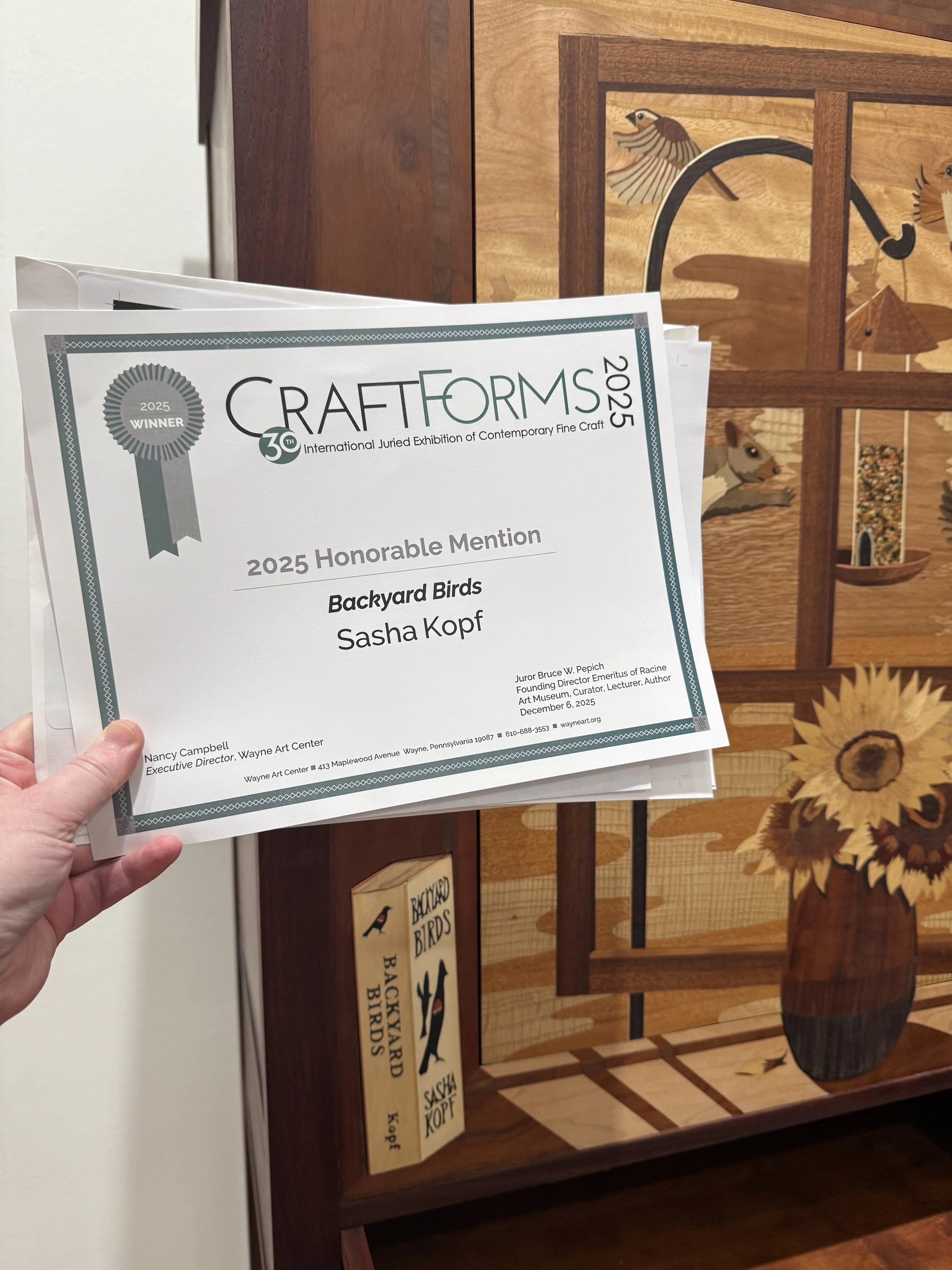 Photo of  my hand holding an Honorable Mention certificate in front of my cabinet