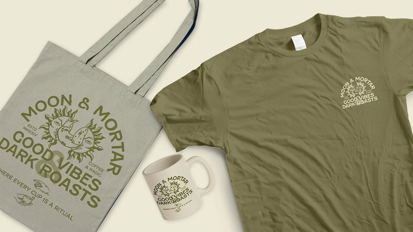 A beige tote bag, an olive green T-shirt, and a white mug all featuring the "Moon & Mortar" logo with a sun and moon design, and says "Good Vibes Dark Roasts".