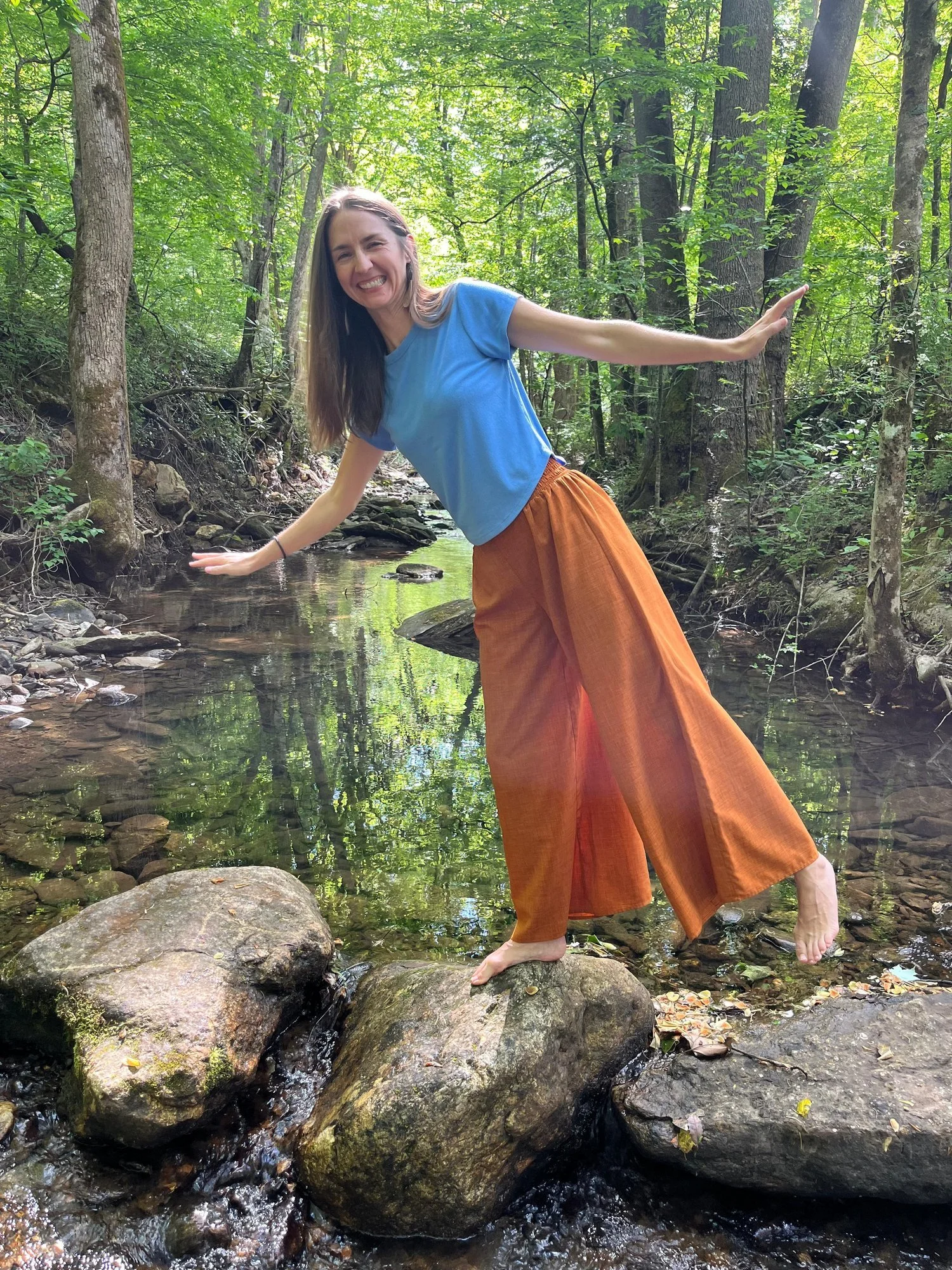 Alex Rice balancing joyfully on creek stones — what thriving looks like after an Ayurvedic cleanse