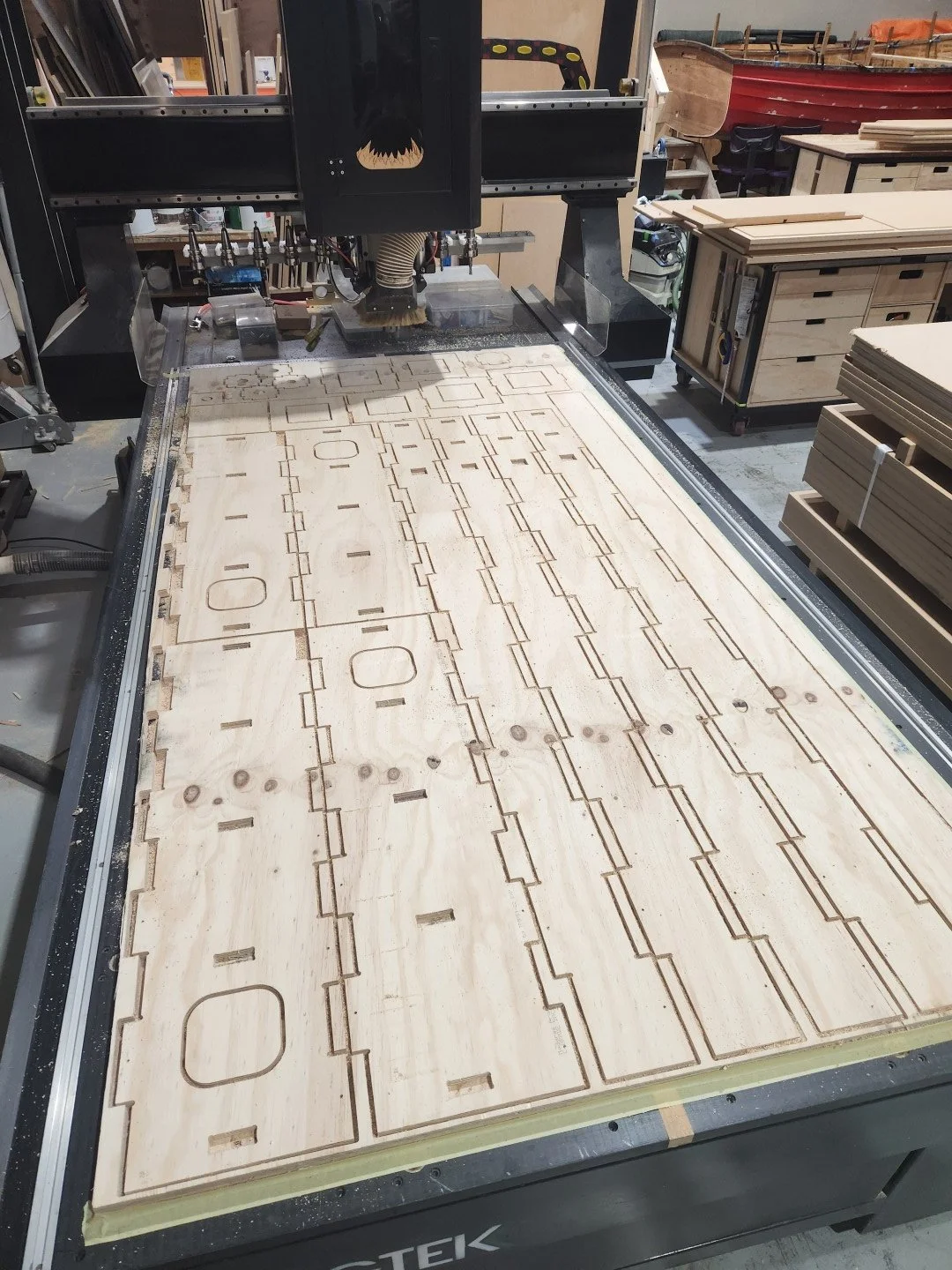 CNC woodworking machine cutting intricate patterns into a large sheet of plywood.