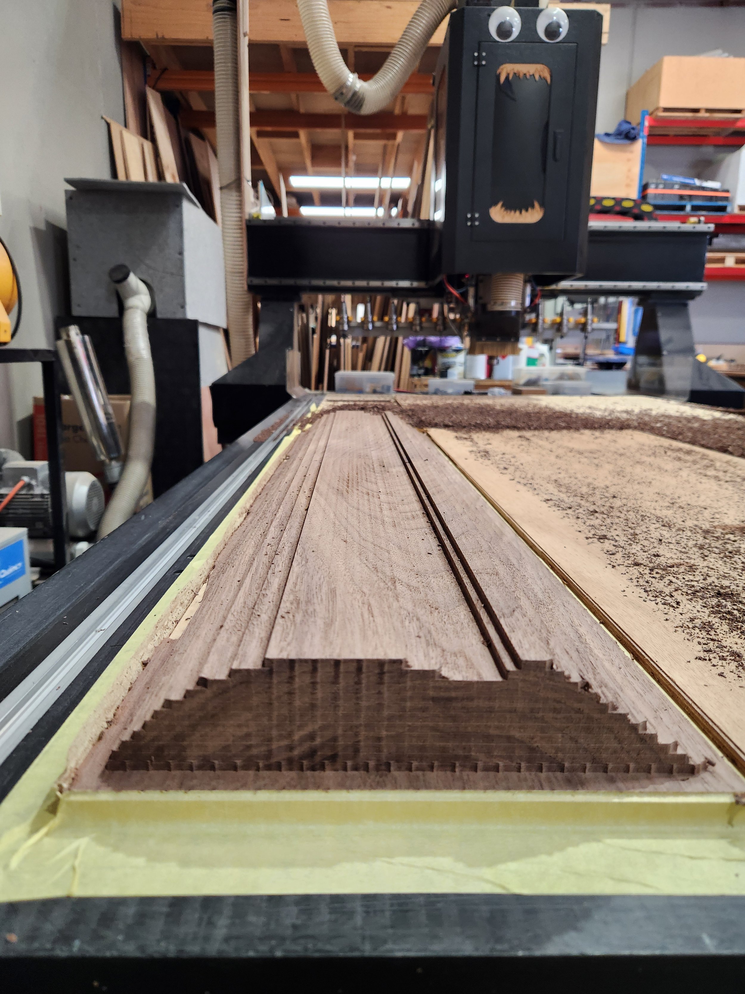 A woodworking router is cutting a detailed groove into a piece of wood in a woodworking shop.