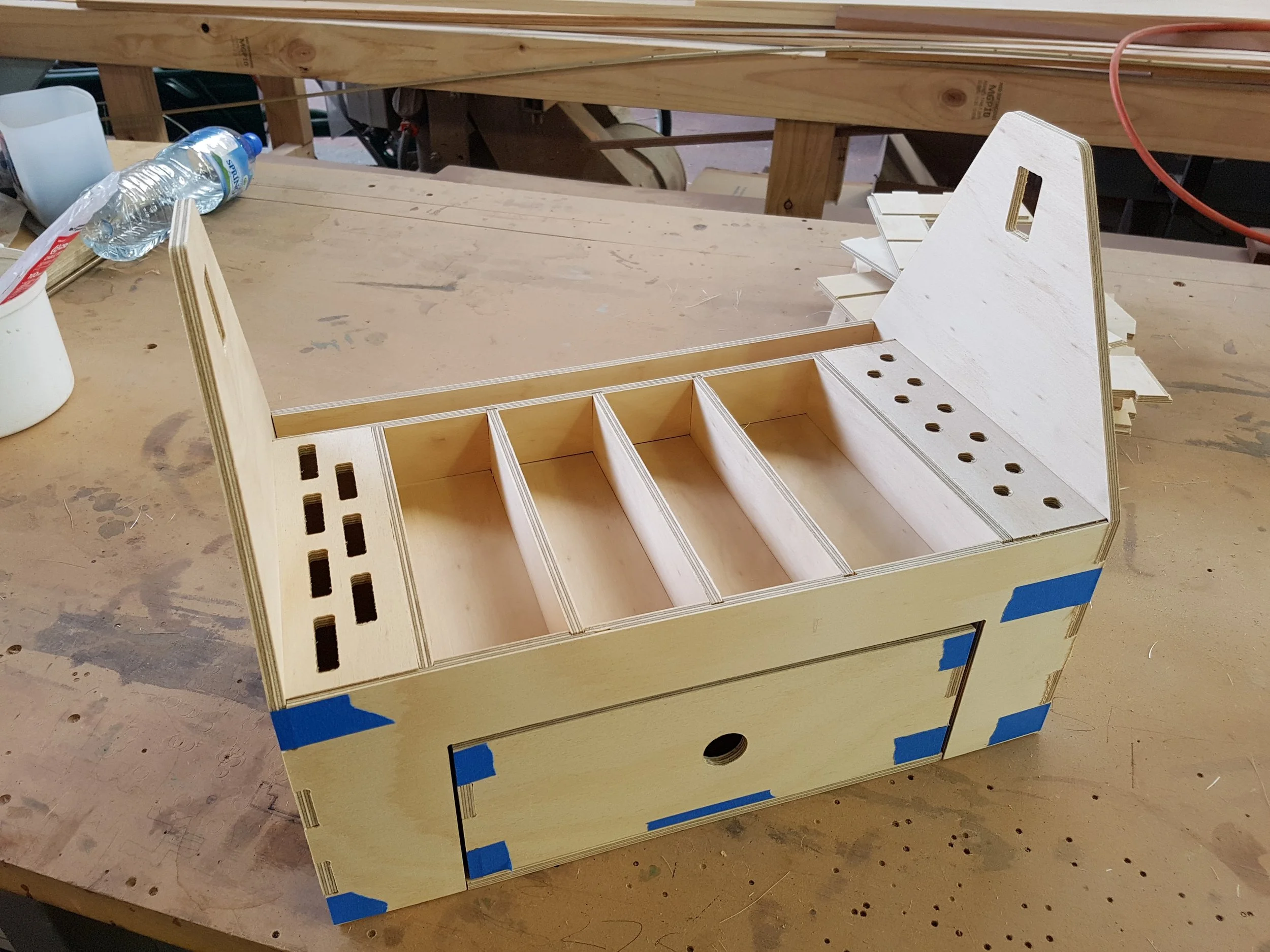 Wooden furniture piece under construction on a workshop table with water bottle and tools visible.