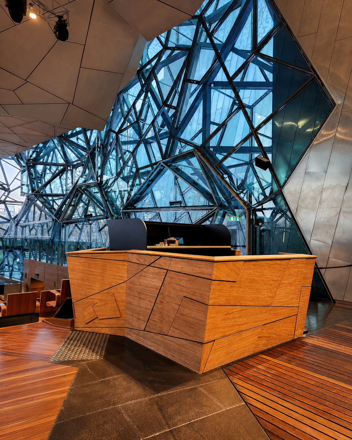 Interior of a modern building with a geometric glass and steel facade, featuring a wooden reception desk and a wooden floor.