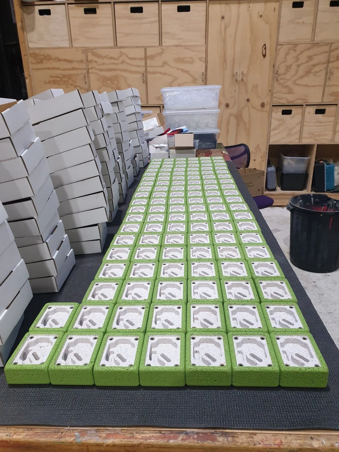 A workspace with numerous small cardboard boxes and green foam blocks on a black surface.