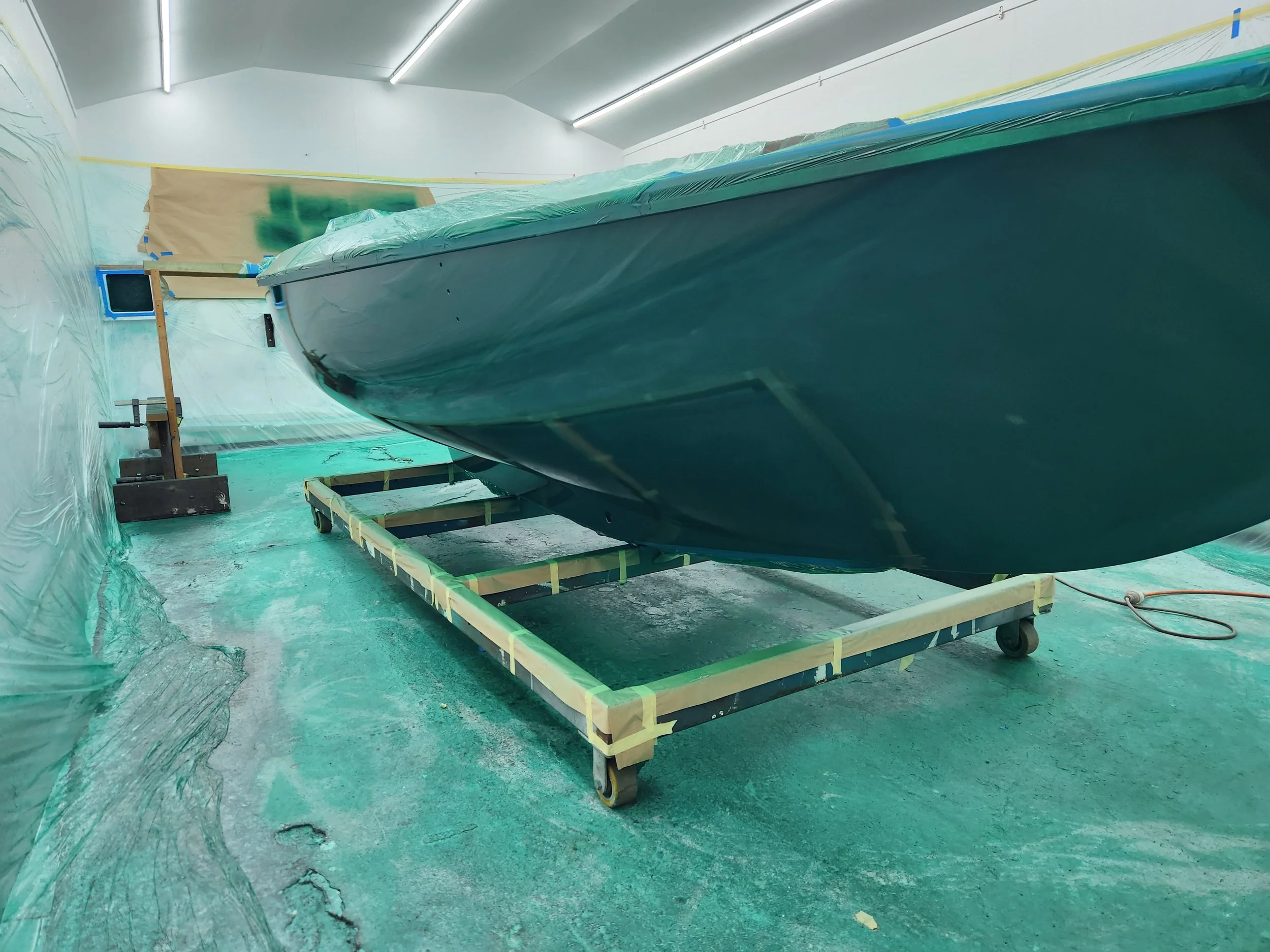 A boat undergoing maintenance or construction inside a workshop, with protective plastic covering and tools around it.