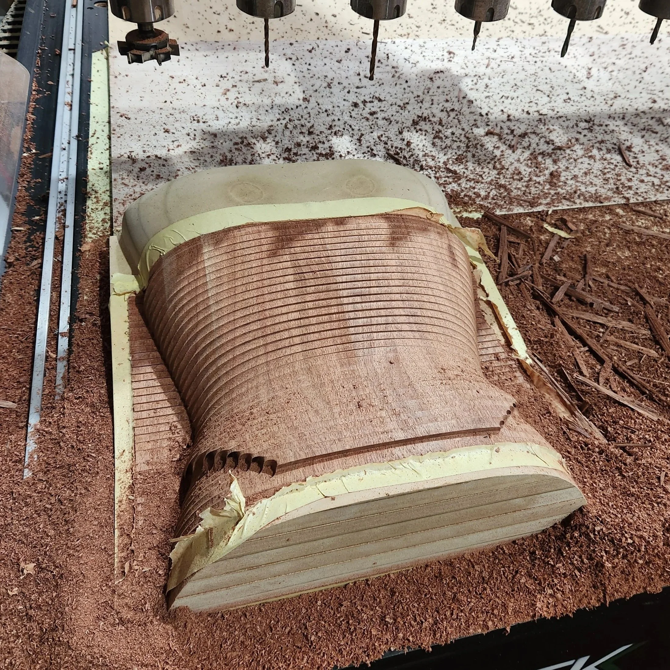 Wooden logs being cut by a machine with several drill bits in a woodworking shop.