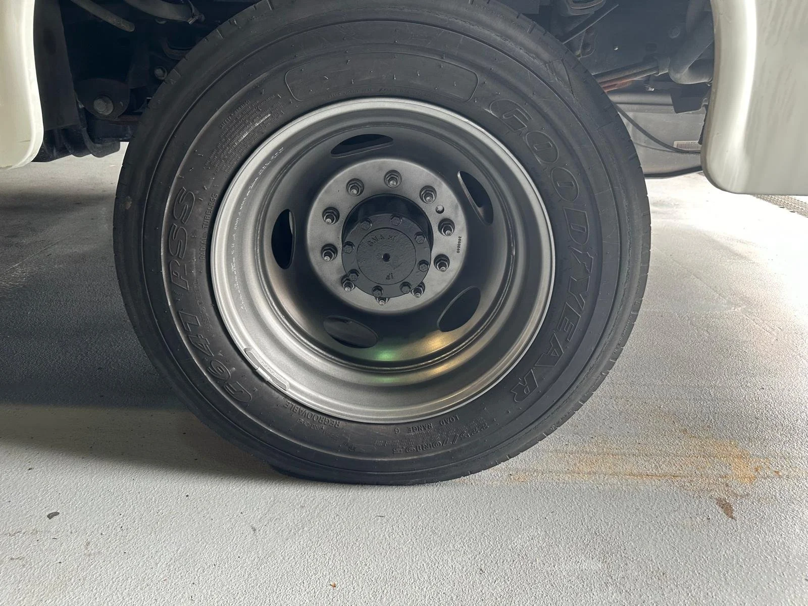 Close-up of a vehicle tire mounted on a steel rim, tires branded Goodyear, on a concrete surface.