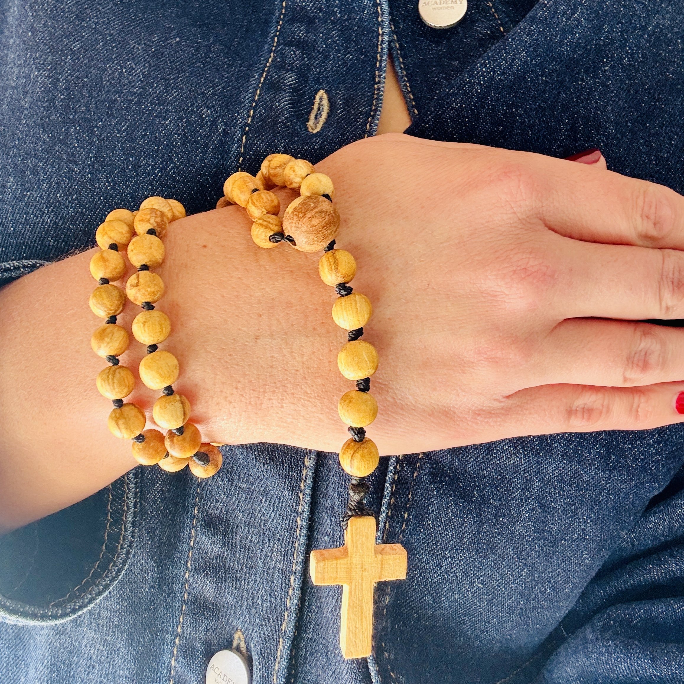 Hand-wrapped Palo Santo rosary with wooden cross beads resting on a wrist, strung with black cord against a denim background.