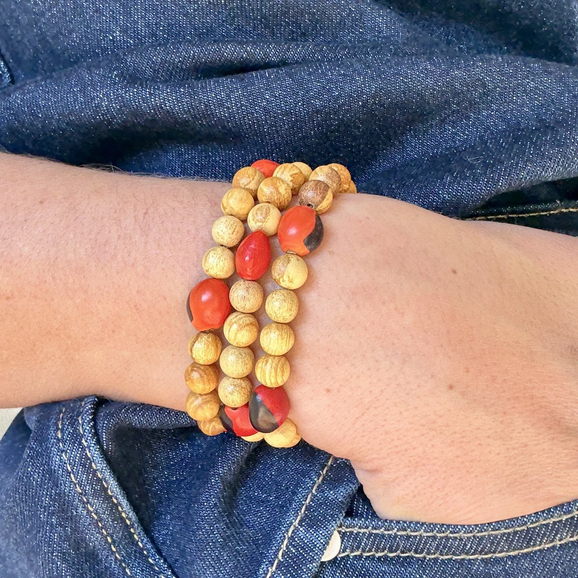 Close-up of a hand wearing a bracelet made from Palo Santo beads and vibrant red and black Huayruro seeds, symbolising protection and ancestral energy.