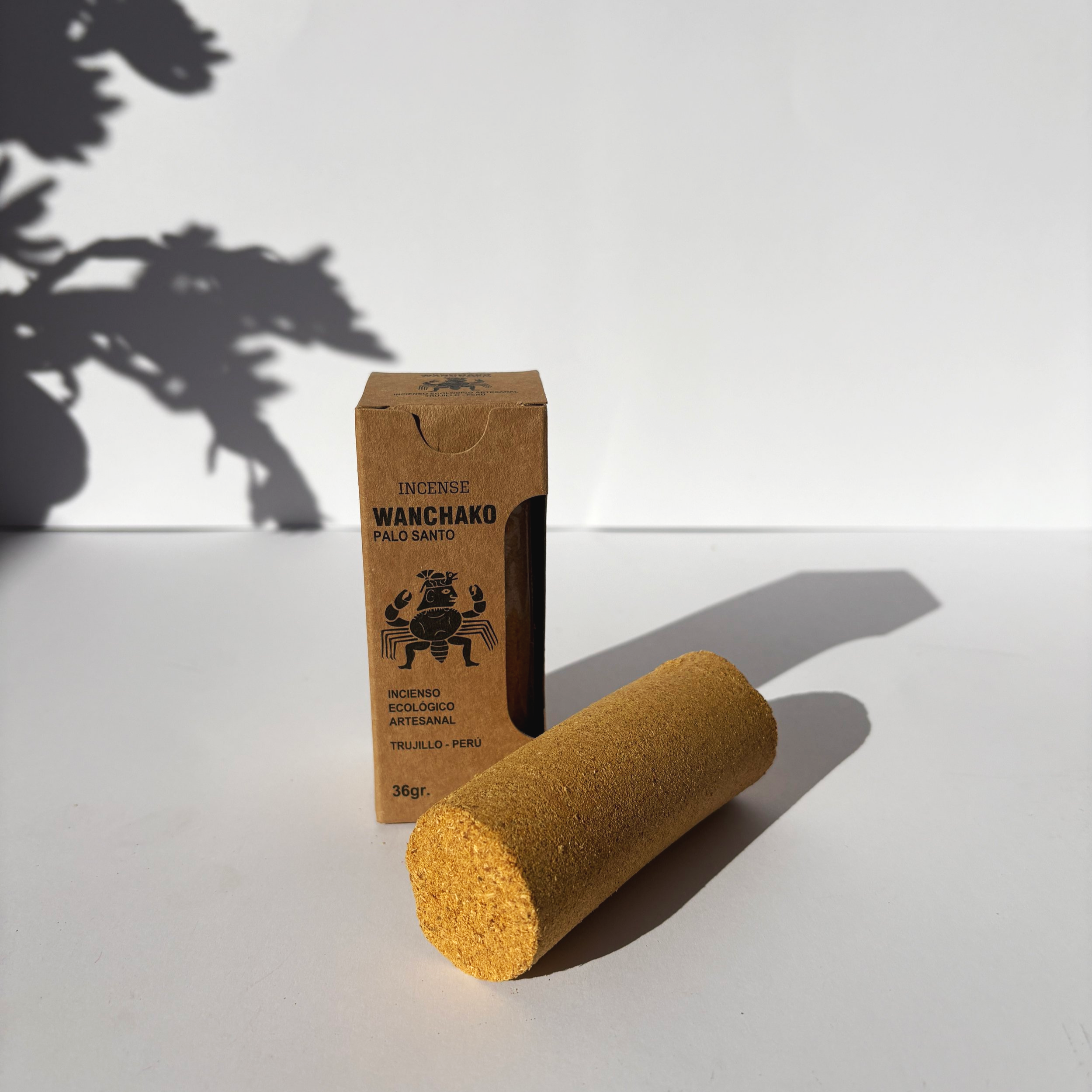 Wanchako Palo Santo ceremonial incense stick placed in front of its kraft box packaging with Incan artwork, captured in natural light.