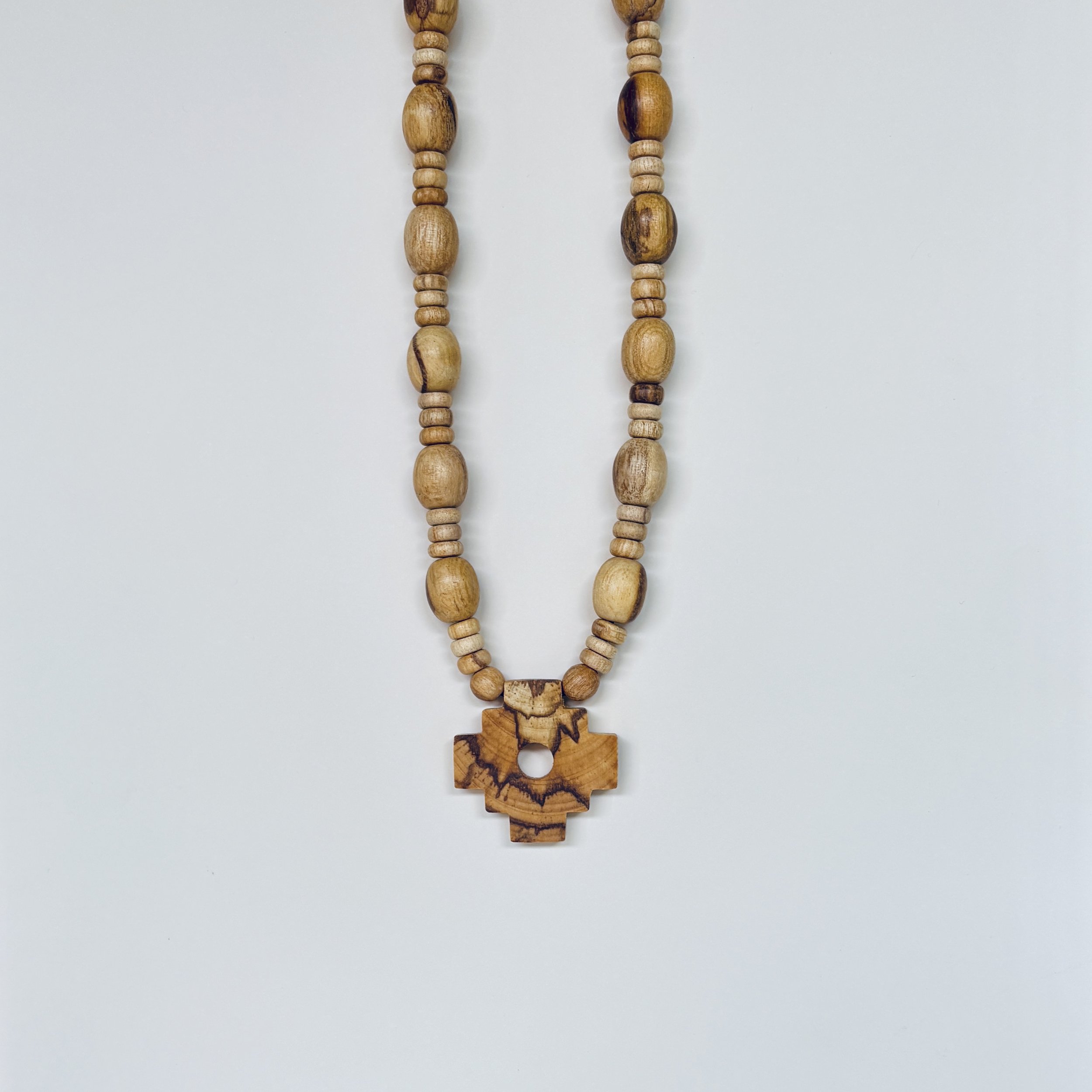 Close-up of a Chakana necklace made from natural Palo Santo wood beads and carved Incan cross pendant, laid flat on white background.