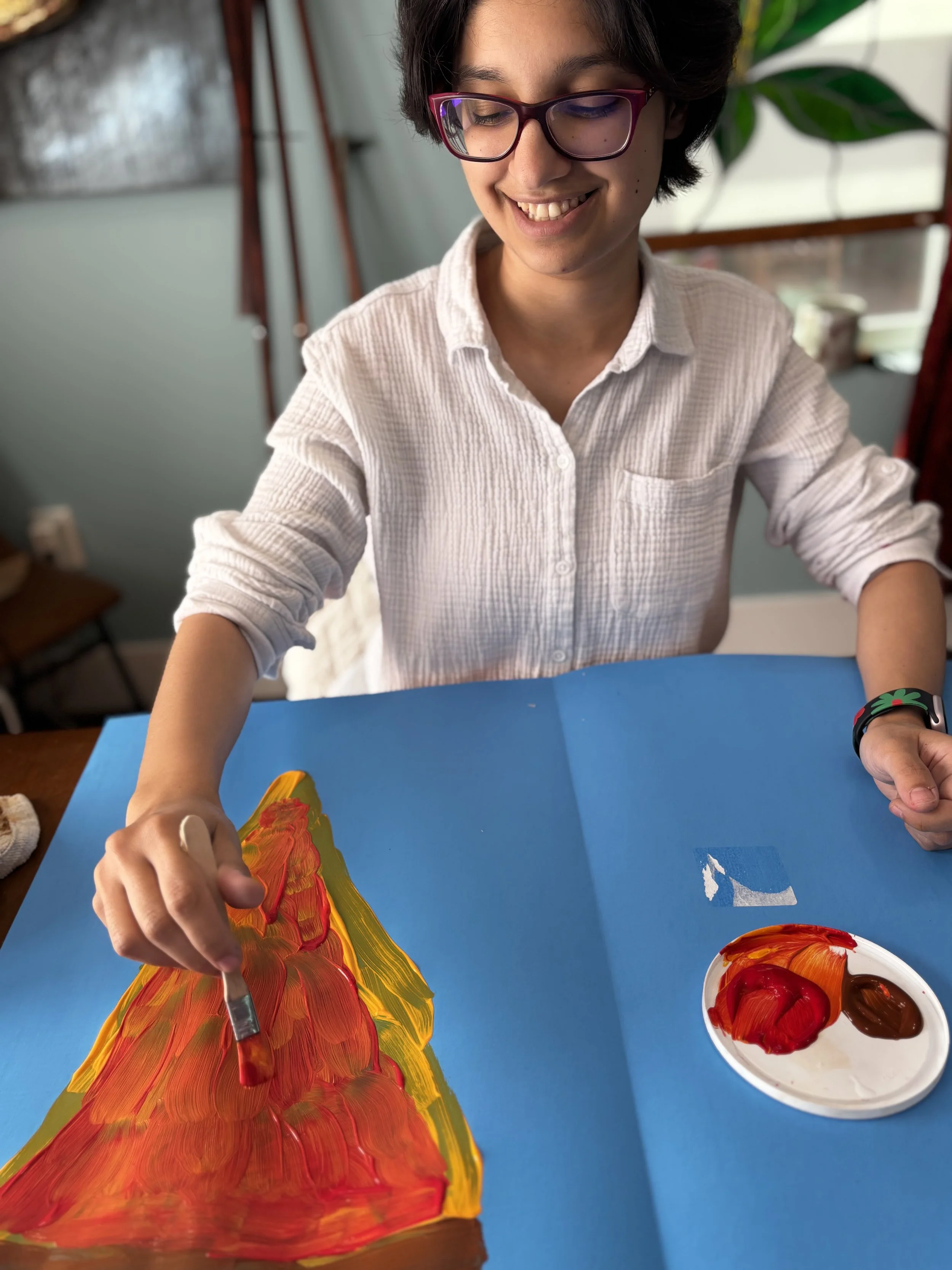 Person with short dark hair and glasses smiling while painting a colorful triangle on a blue background.