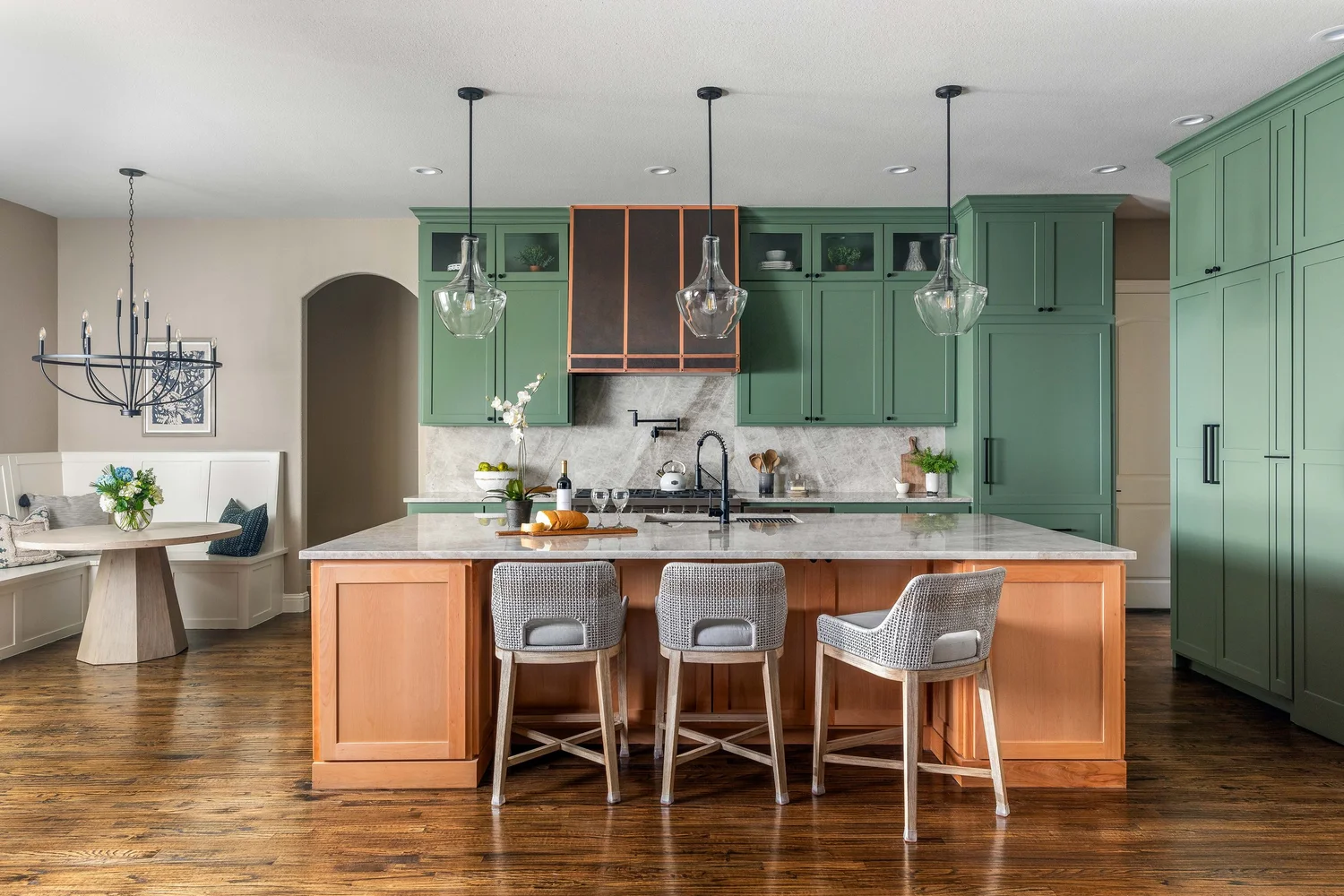 Kitchen with green cabinetry, a marble-topped island and a built-in dining nook, designed by Ashley Pate Interior Design