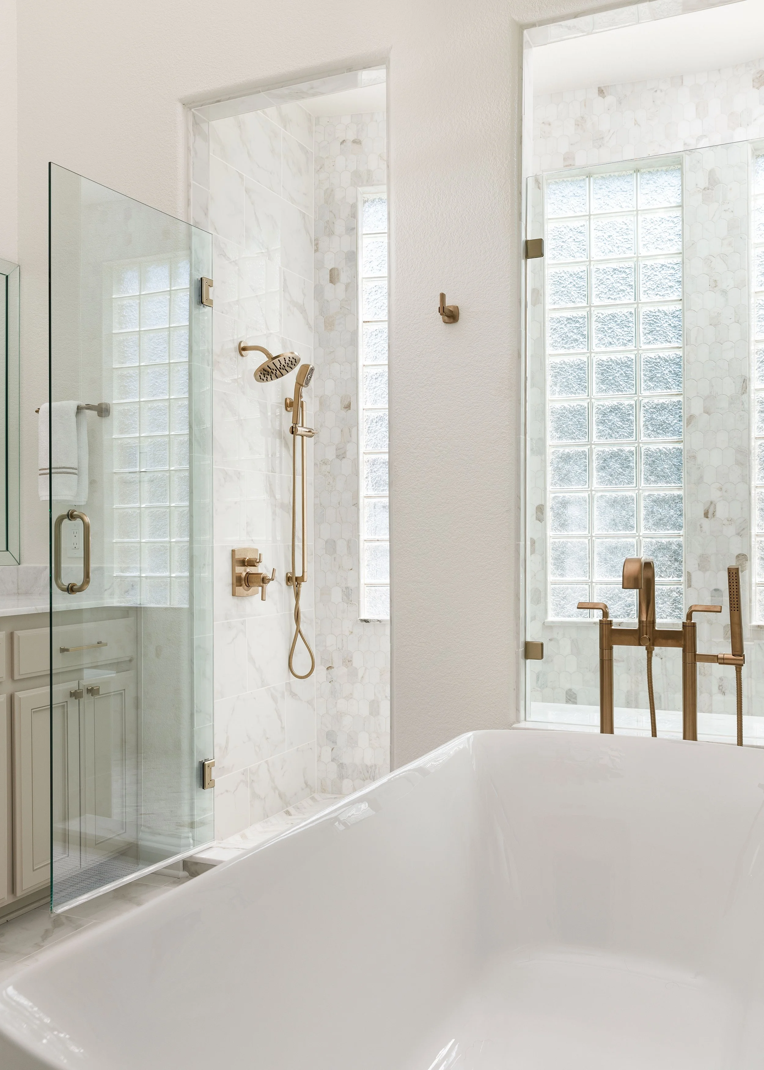 Modern bathroom with a bathtub, glass shower enclosure, brass fixtures, and tufted glass block windows for natural light.