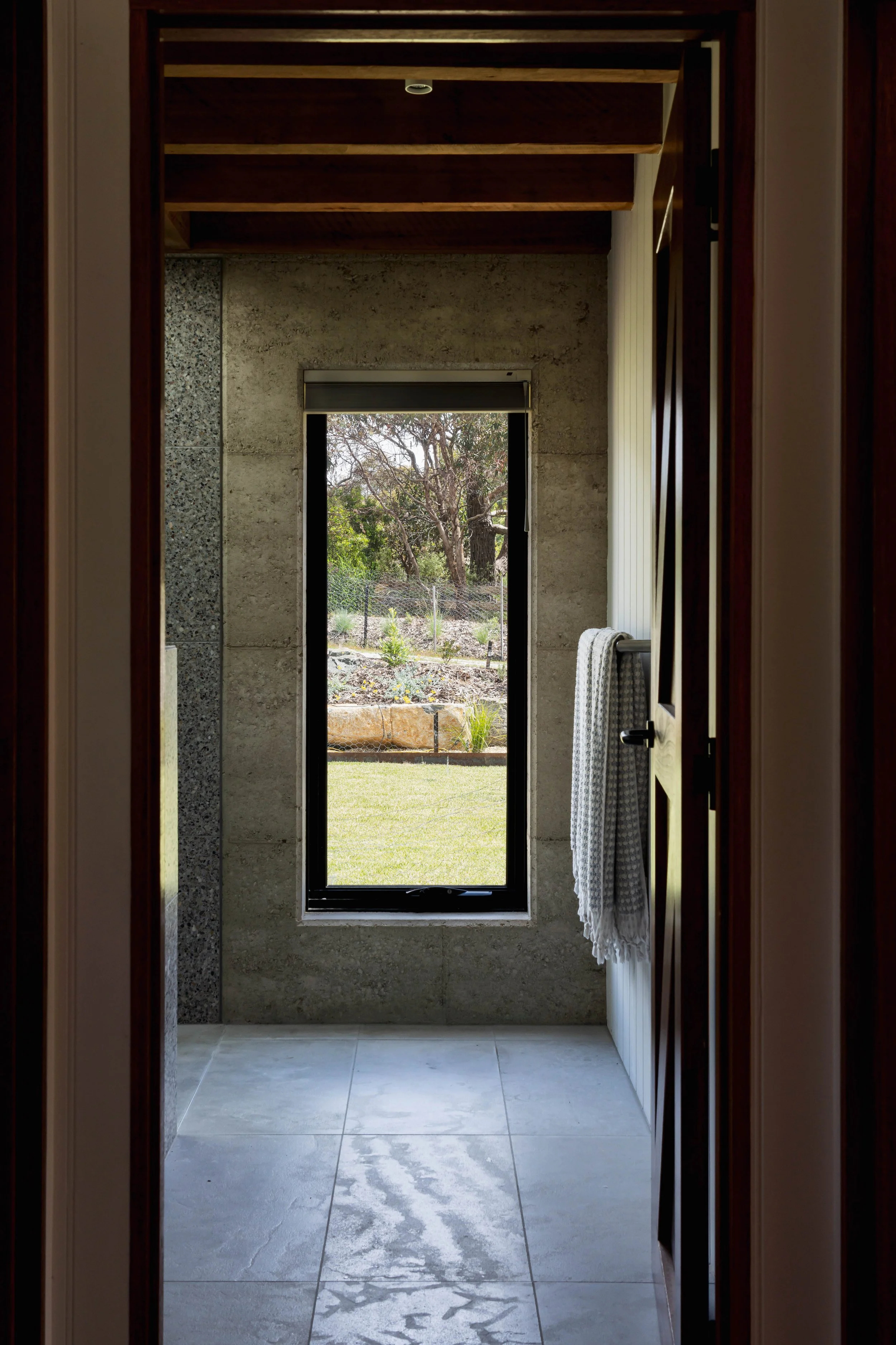 Modern interior with rammed earth wall, large window view to garden, and tiled floor.