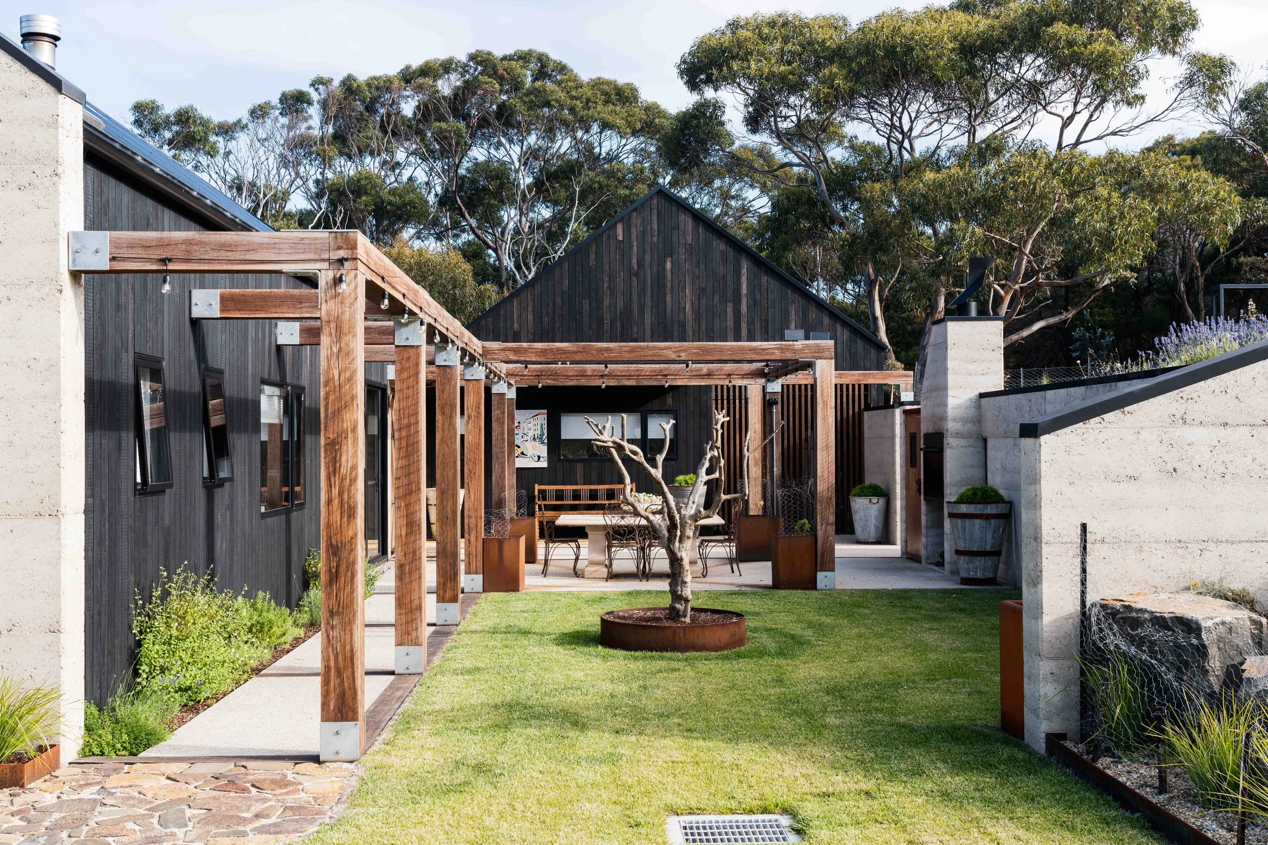 Rural dream home courtyard with rammed earth, Shou Sugi Ban cladding and ironbark arbor in Bicheno, Tasmania by Loubser Workshop