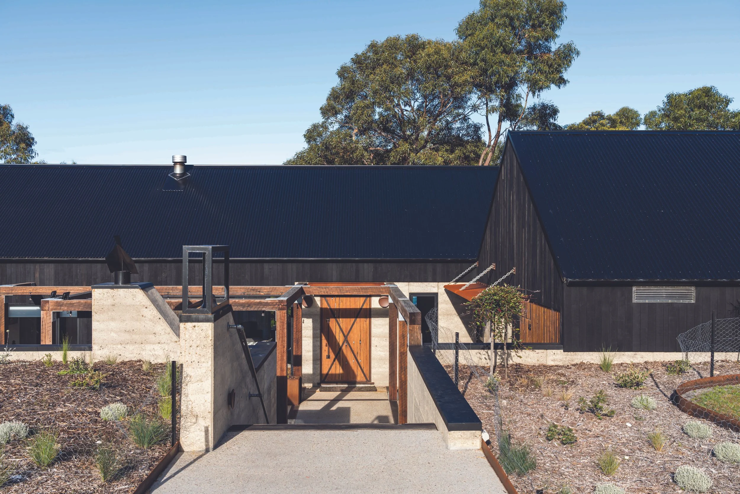 Rural dream home entry pathway with sculptural rammed earth, Shou Sugi Ban cladding and ironbark arbor in Bicheno, Tasmania by Loubser Workshop