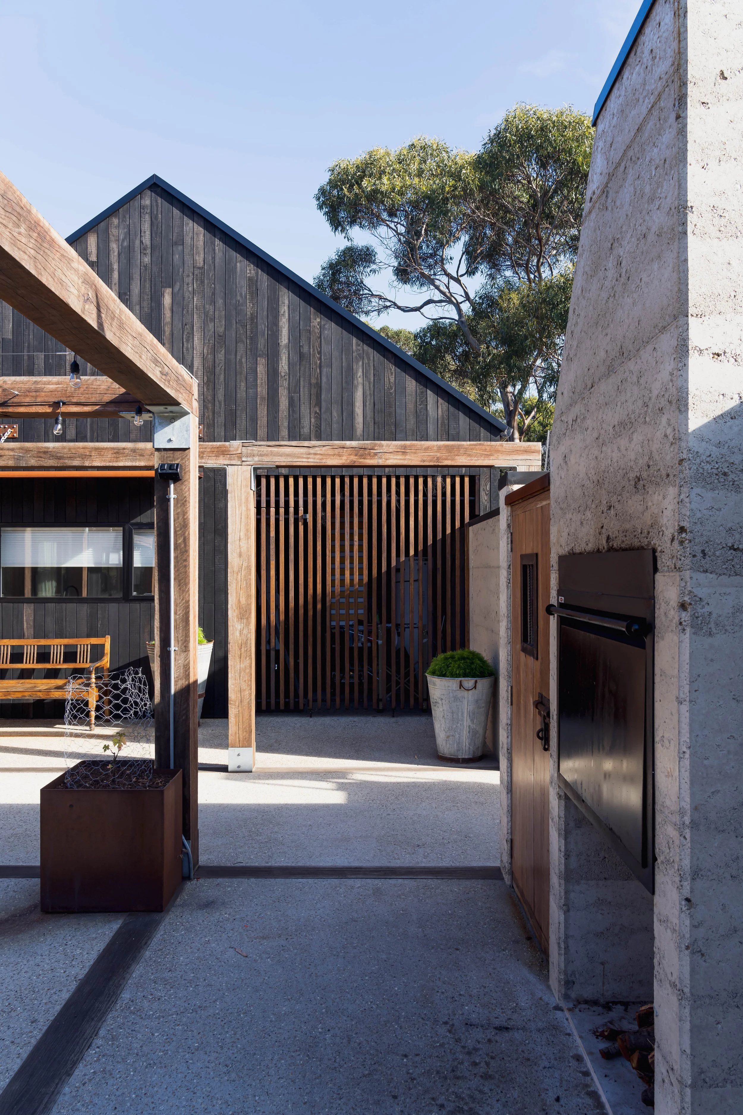 Rural dream home courtyard with rammed earth, Shou Sugi Ban cladding and ironbark arbor in Bicheno, Tasmania by Loubser Workshop