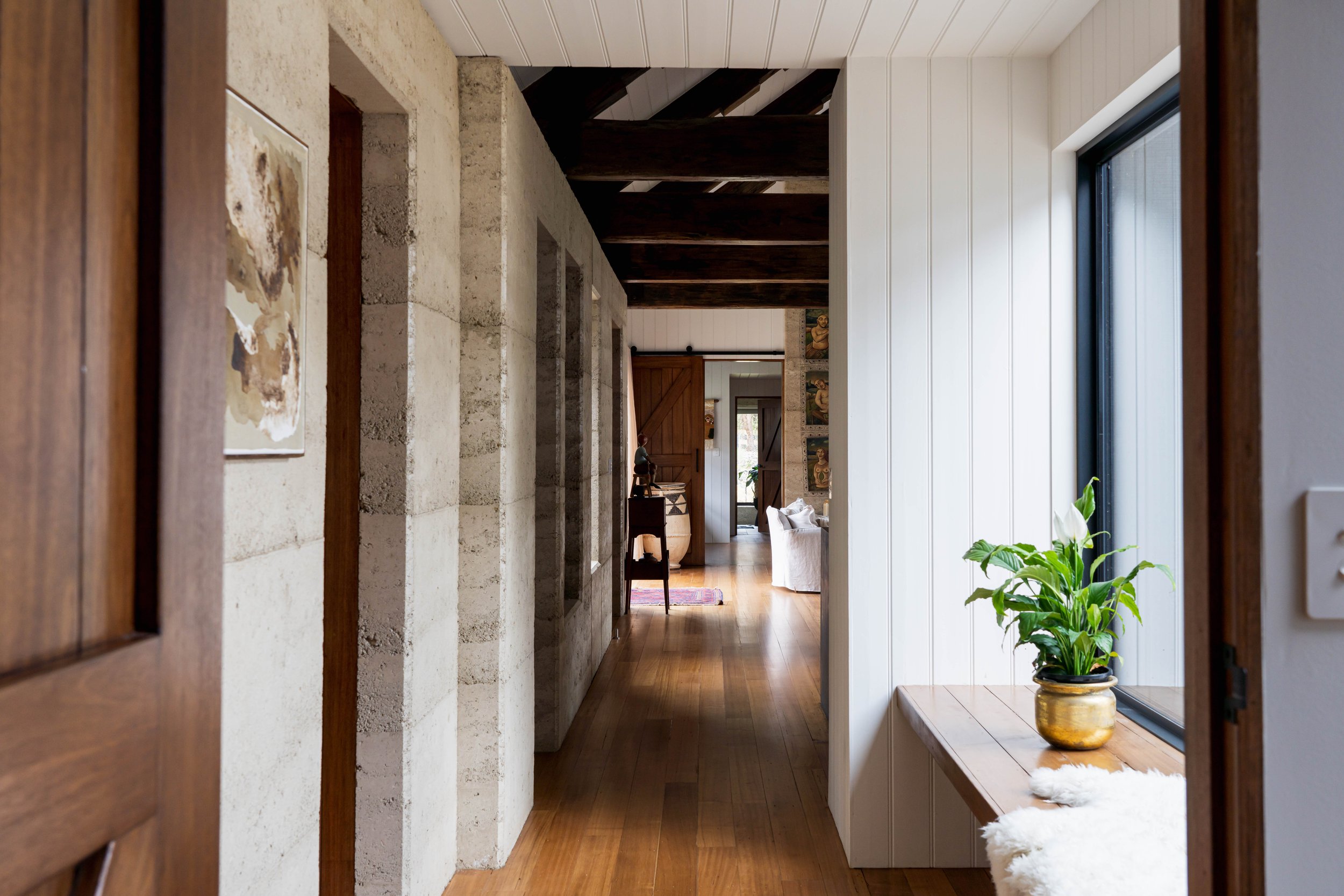 Rural dream home hallway interior with rammed earth and reclaimed wharf timber trusses in Bicheno, Tasmania by Loubser Workshop