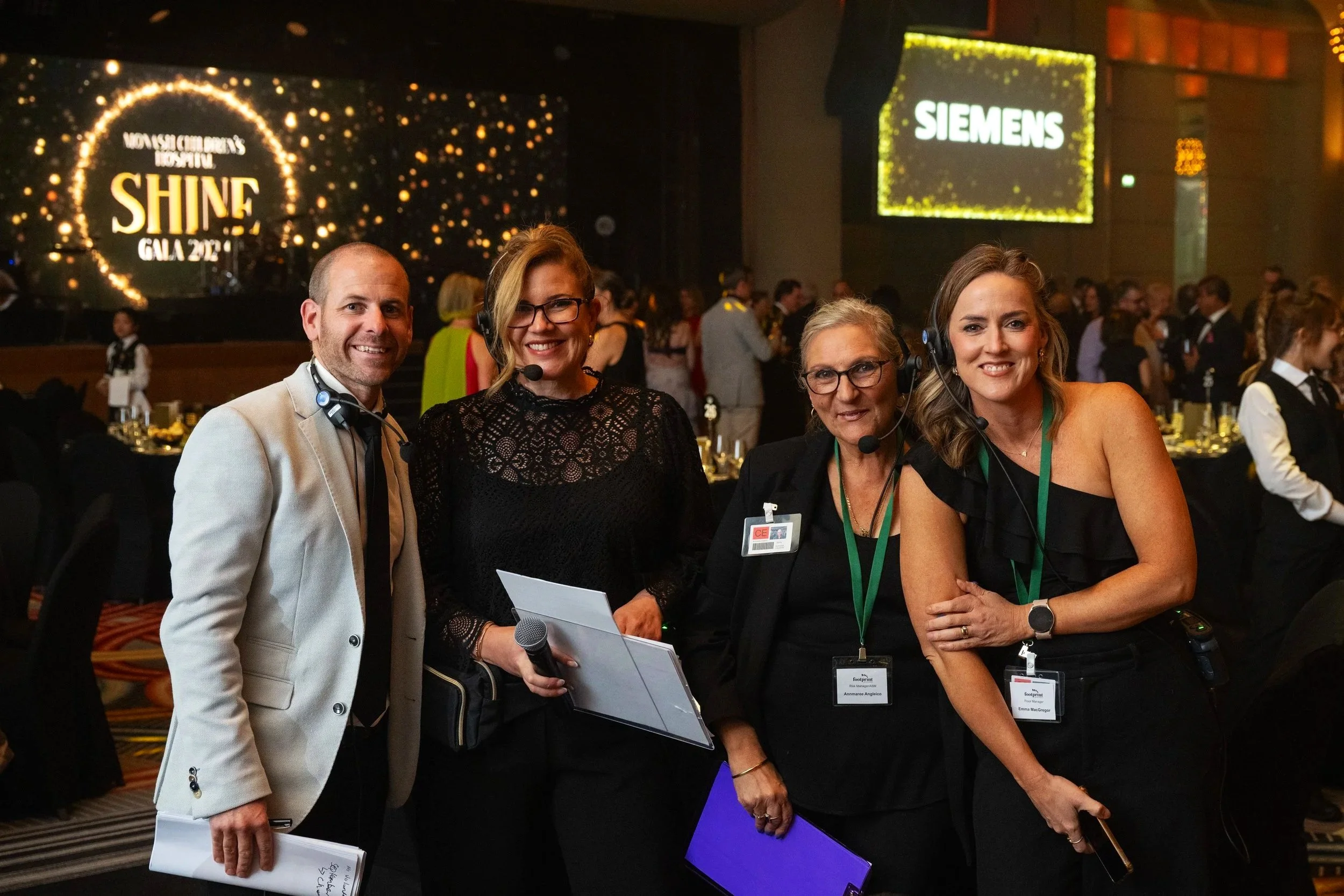 Four people wearing headsets standing together at an event with a large screen that says "SHINE Gala 2021".
