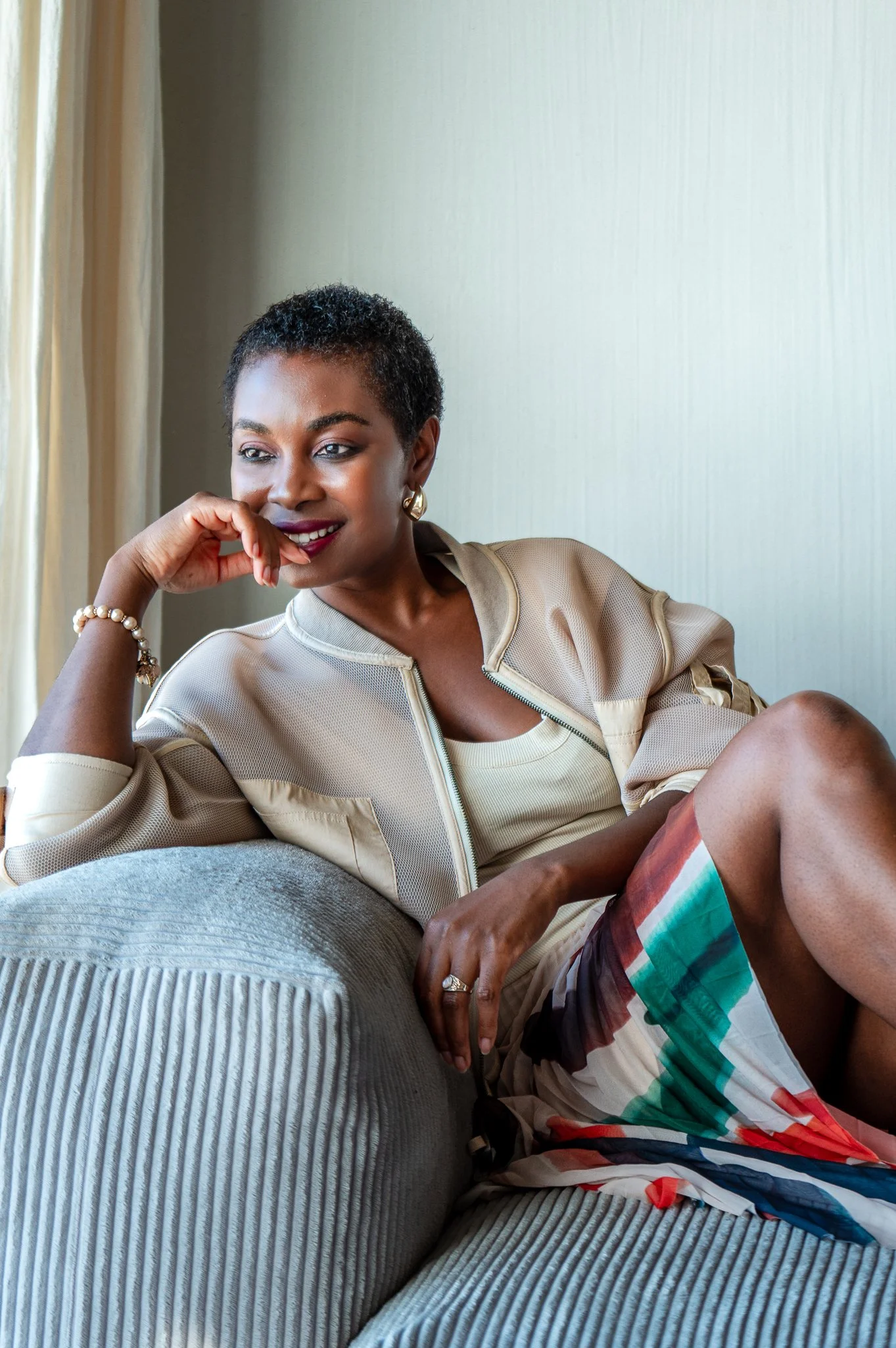A Portrait of Faith Müller sitting on a sofa, steering out the window with a smile on her face.