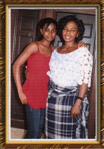 An old photo of Faith Müller and her mother  posing for a photo. Younger Faith Müller is wearing a modern spaghetti strap red top and denim trousers and her mum is wearing a traditional white lace blouse and checkered blue & white wrapper